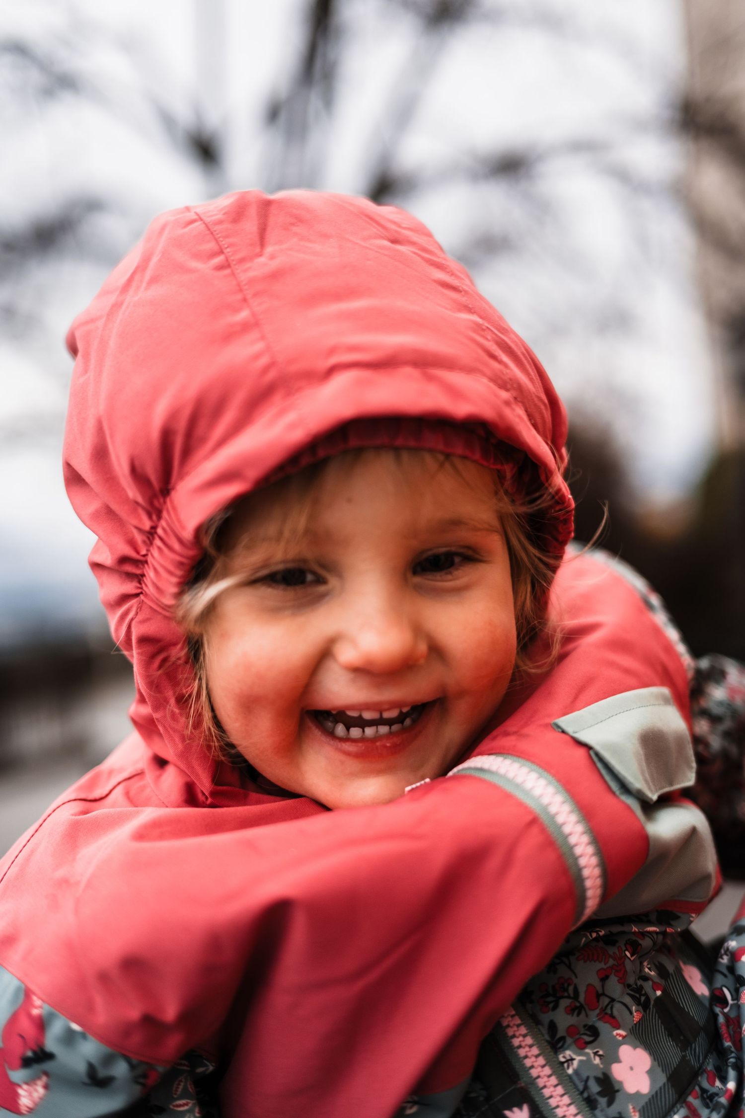 Child in a red winter coat smiling and playing in the snow.
