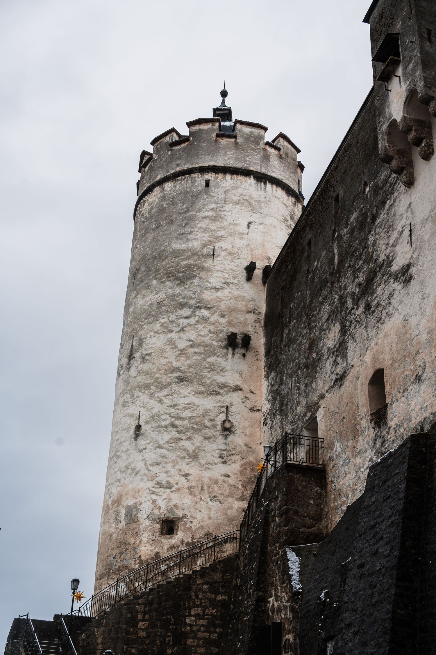 Ancient stone castle tower with white walls and dark base against an overcast sky.