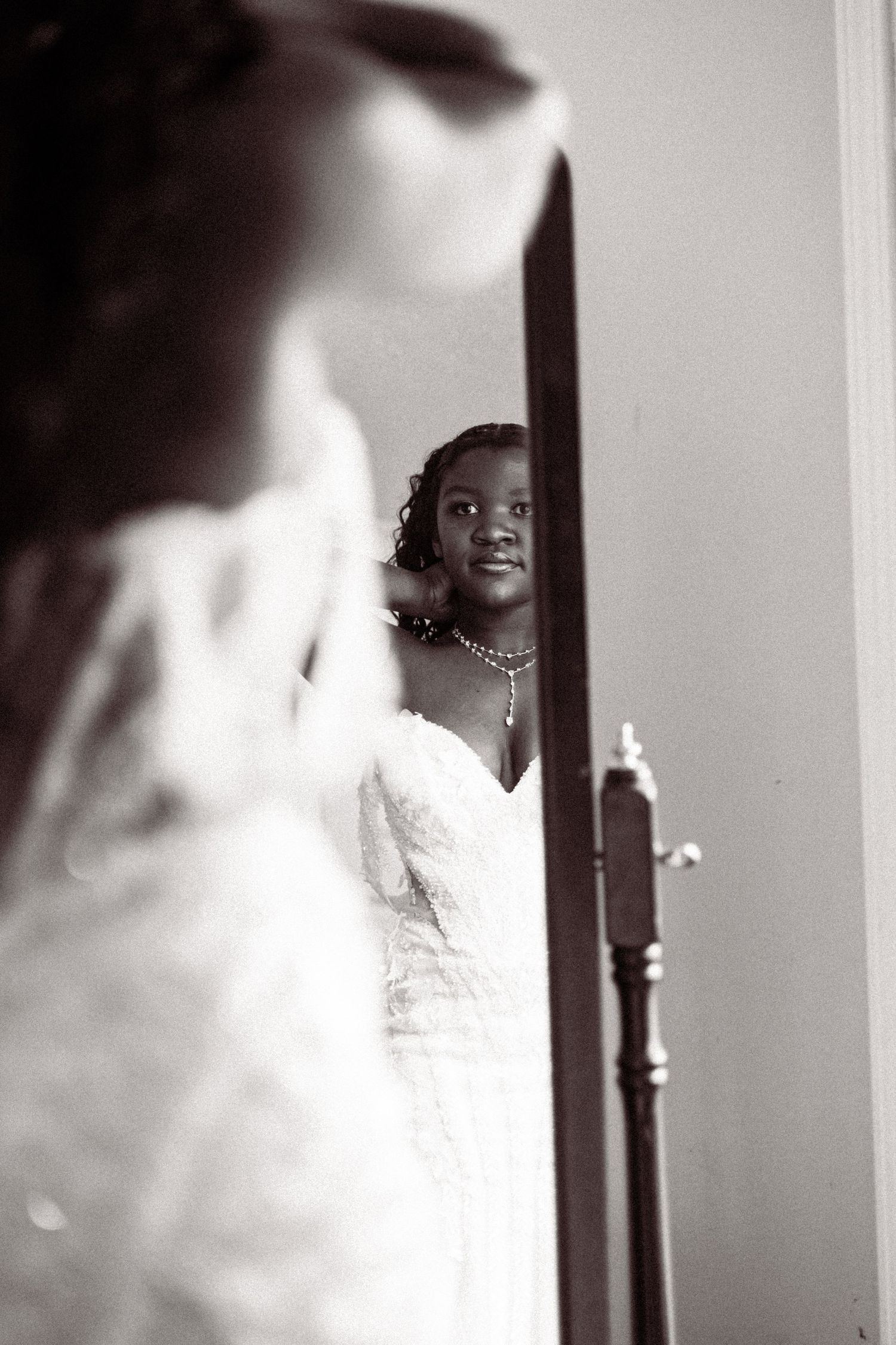 Bride in lace wedding gown smiling at her reflection in a full-length mirror.