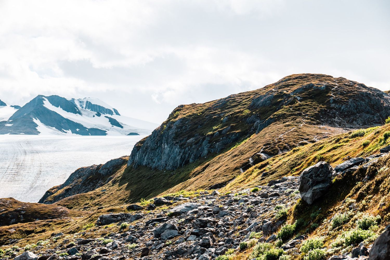 Rugged mountain landscape with snow-capped peaks and rocky terrain against a bright sky in summer.