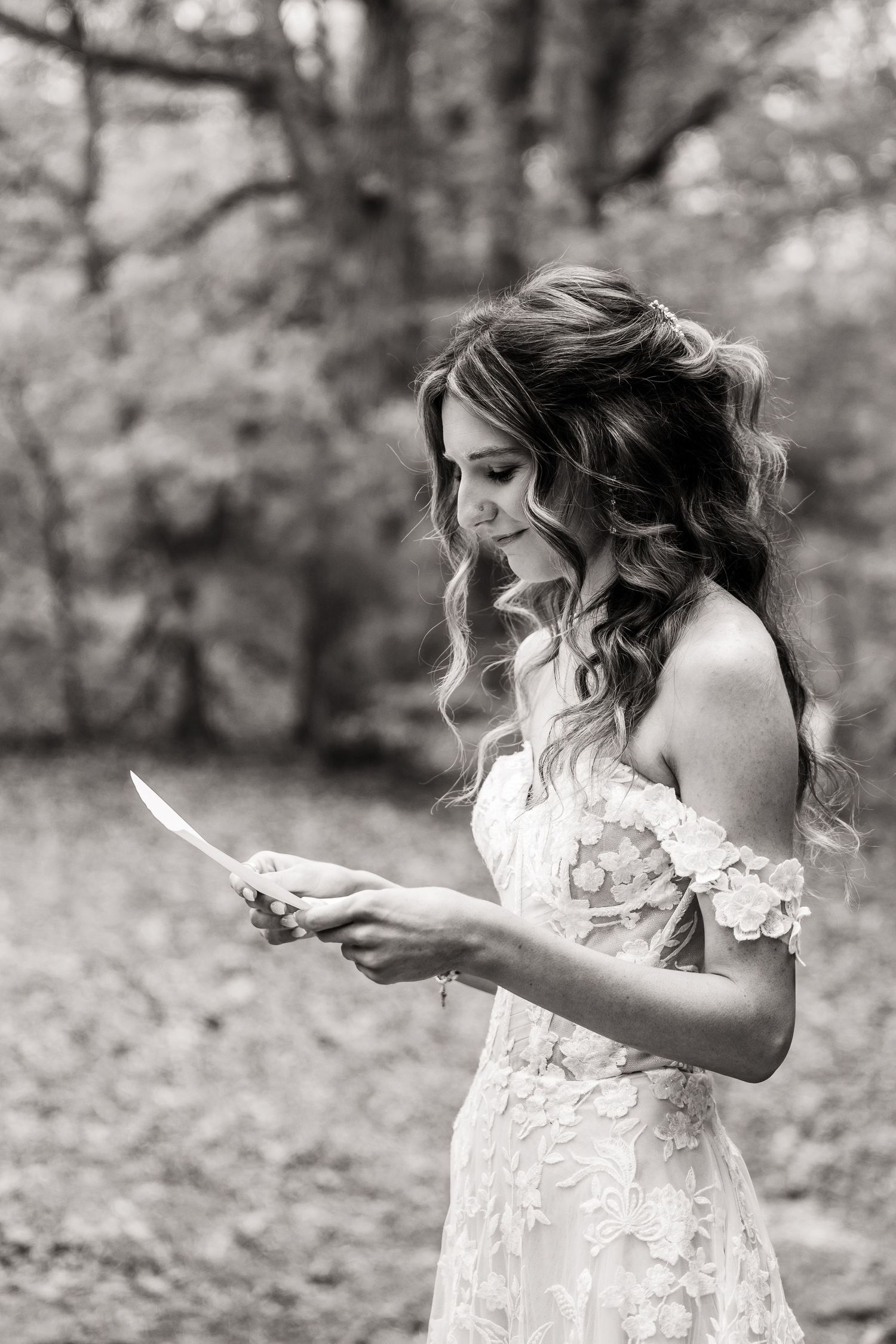 Bride in lace dress reads letter outdoors in black and white portrait.