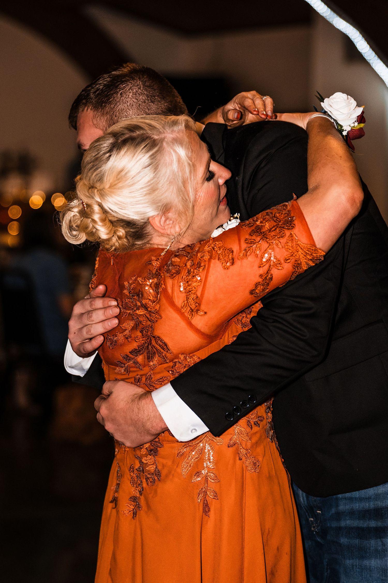 Wedding guests dancing in formal attire with woman in vibrant orange dress at reception.