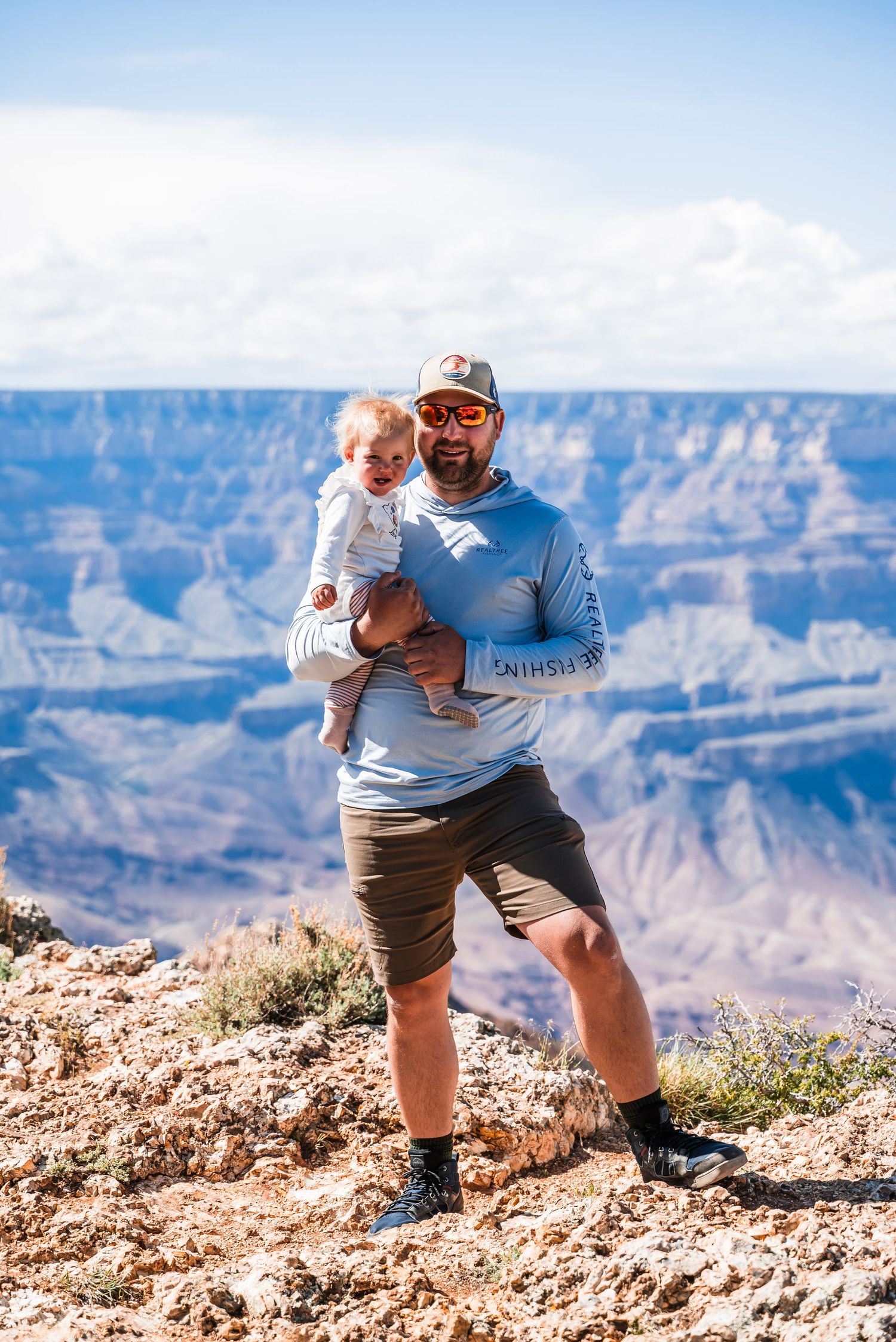 Visitors enjoy a sunny day at the Grand Canyon's rim, with the vast canyon and blue sky in the background.