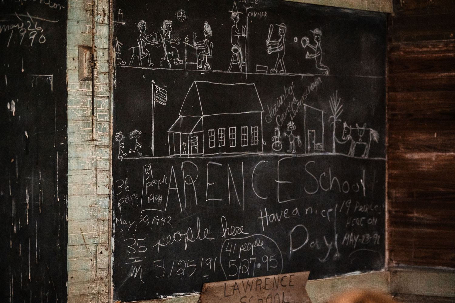 Old black chalkboard with faded chalk writings and drawings on classroom wall.