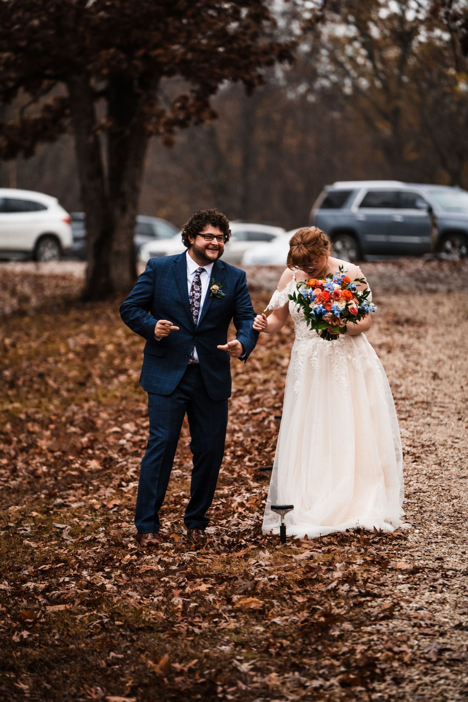 Couple walking and laughing together on leaf-covered path during fall wedding.