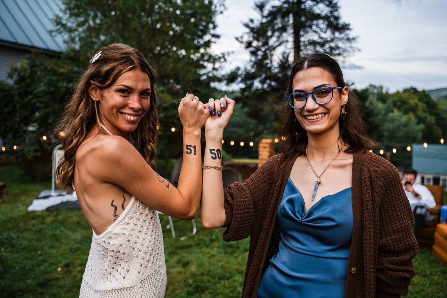 Two guests celebrate during an outdoor wedding reception with string lights in the background.