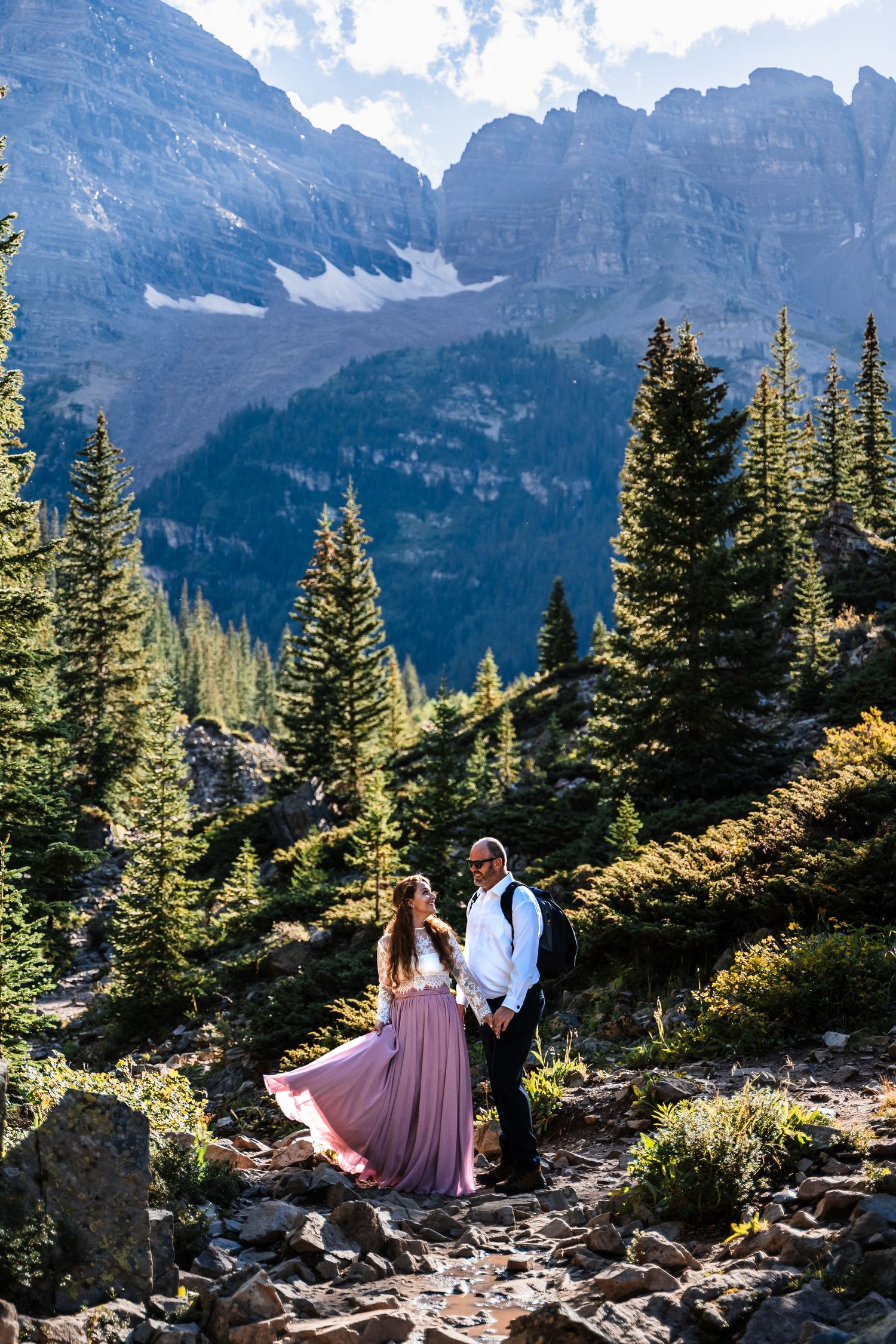 A romantic mountain photoshoot with dramatic rocky peaks and evergreen trees in the background.