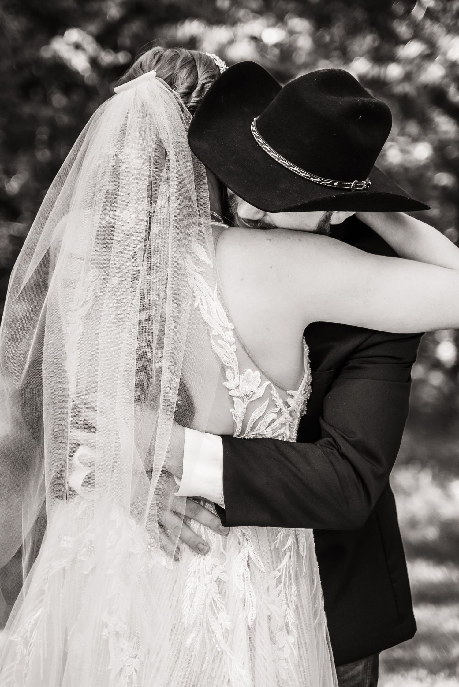 A romantic black and white wedding photo showing an intimate embrace, with the bride's veil flowing in soft focus.