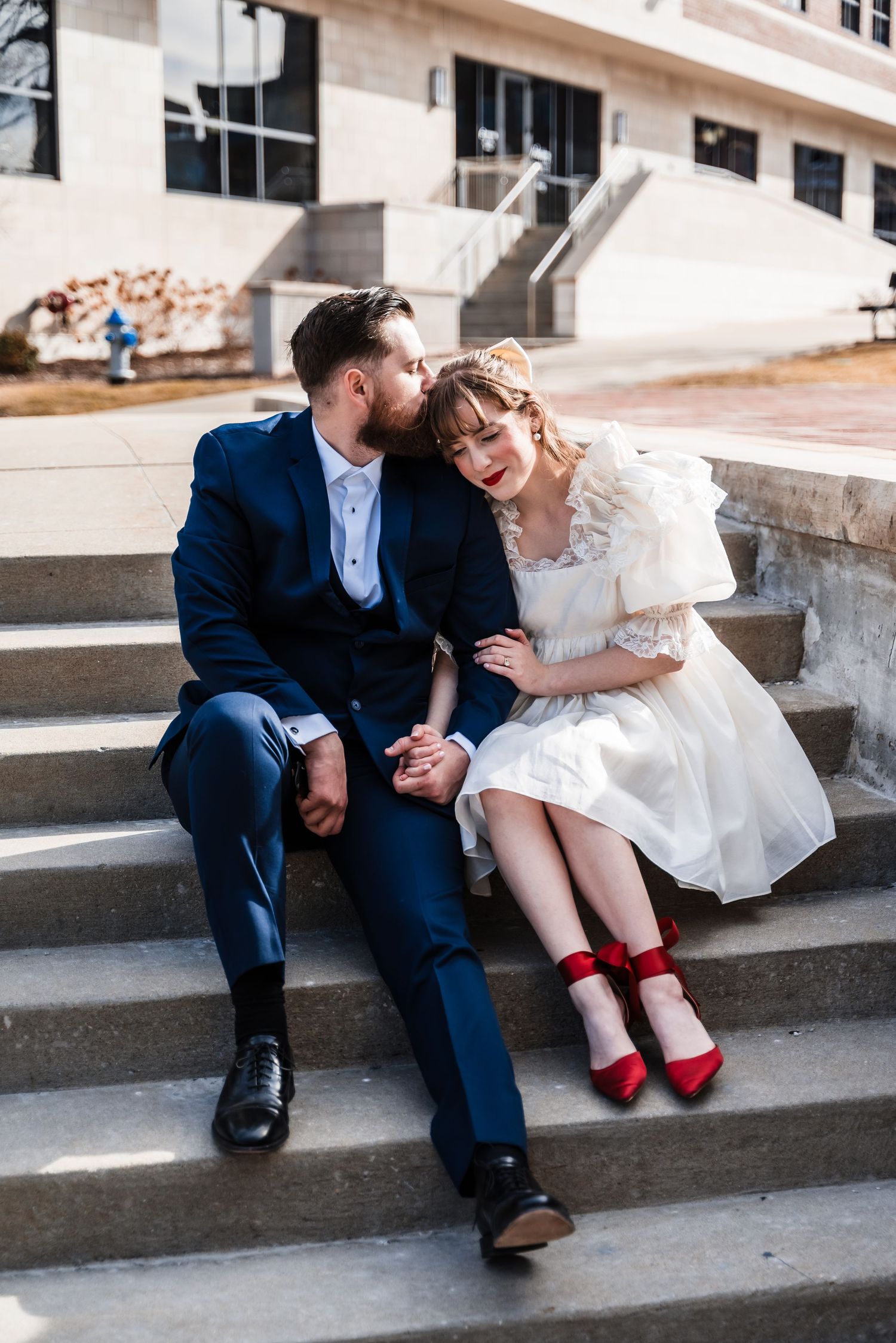A couple in blue suit and white dress sharing an intimate moment on urban steps.