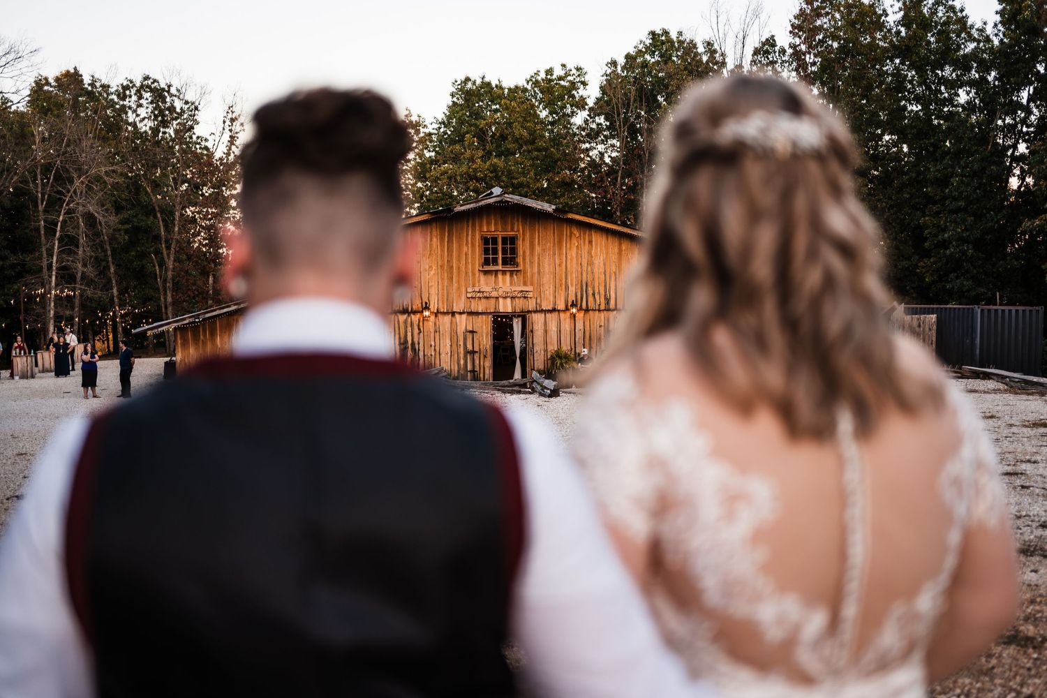 A couple faces a rustic barn building during their autumn wedding photoshoot.