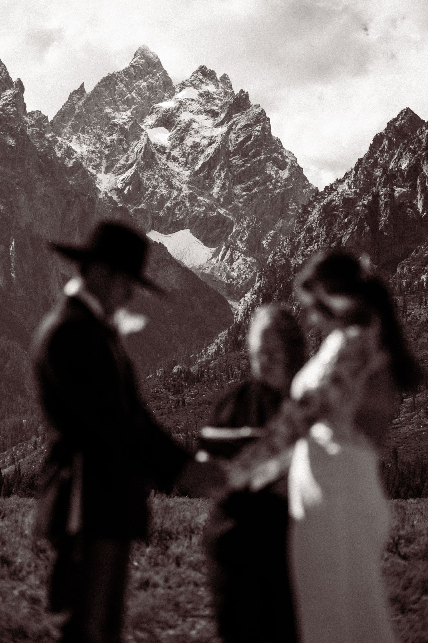 Silhouettes of a couple dancing in front of majestic snow-capped mountain peaks in black and white.