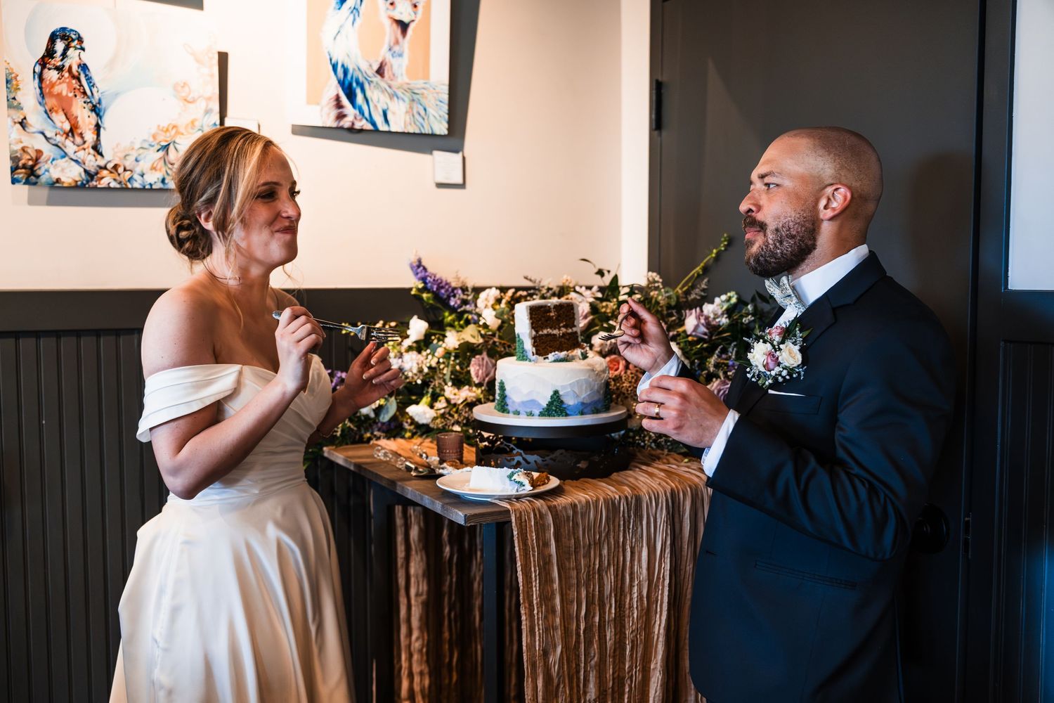 Bride and groom laugh together while cutting mountain-themed wedding cake at reception.