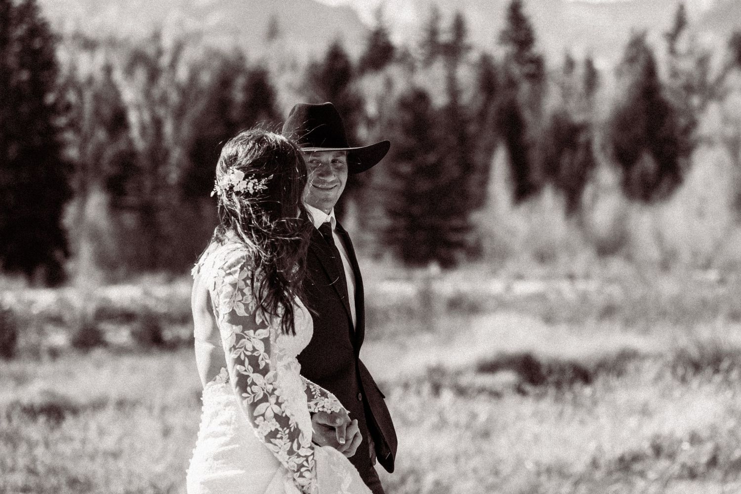 A black and white photo of newlyweds in formal attire standing together against a mountain landscape.