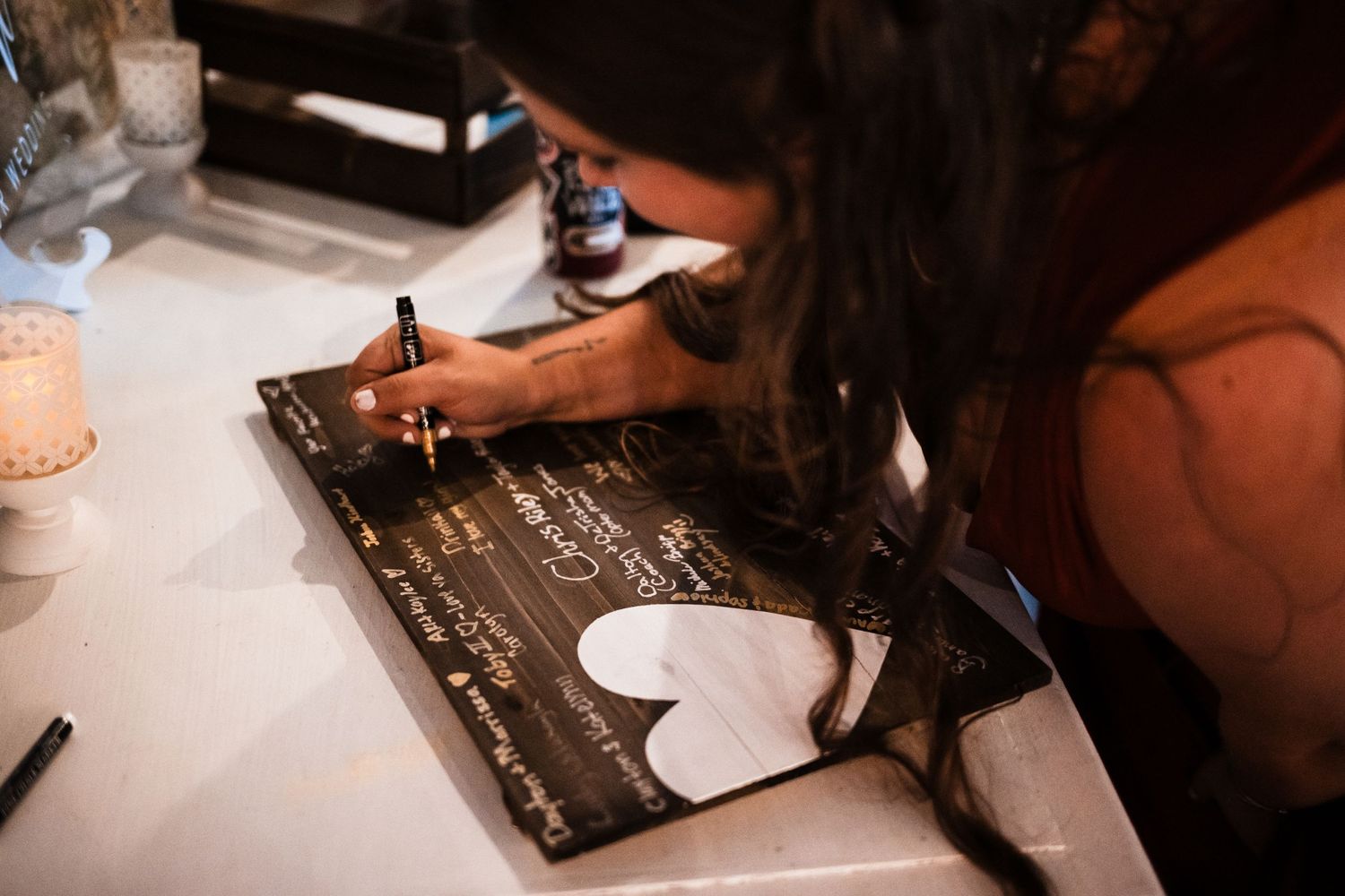 Guest signing wedding guestbook or memory book with black pen at reception table.