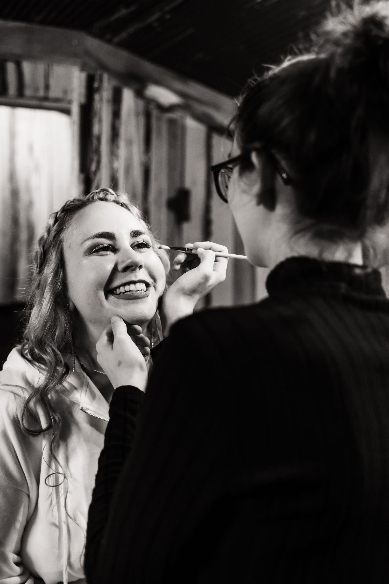 Makeup artist applies cosmetics to a smiling woman during wedding preparations.