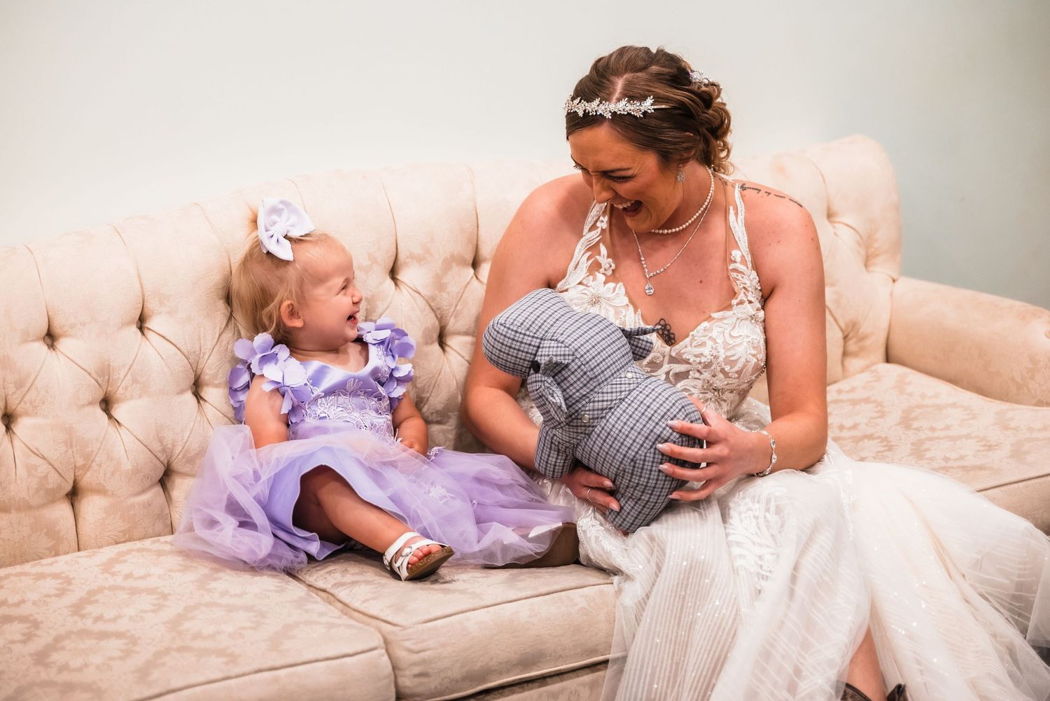 A tender family moment shared on an elegant beige tufted couch as they bond with a newborn in gingham and lavender outfits.