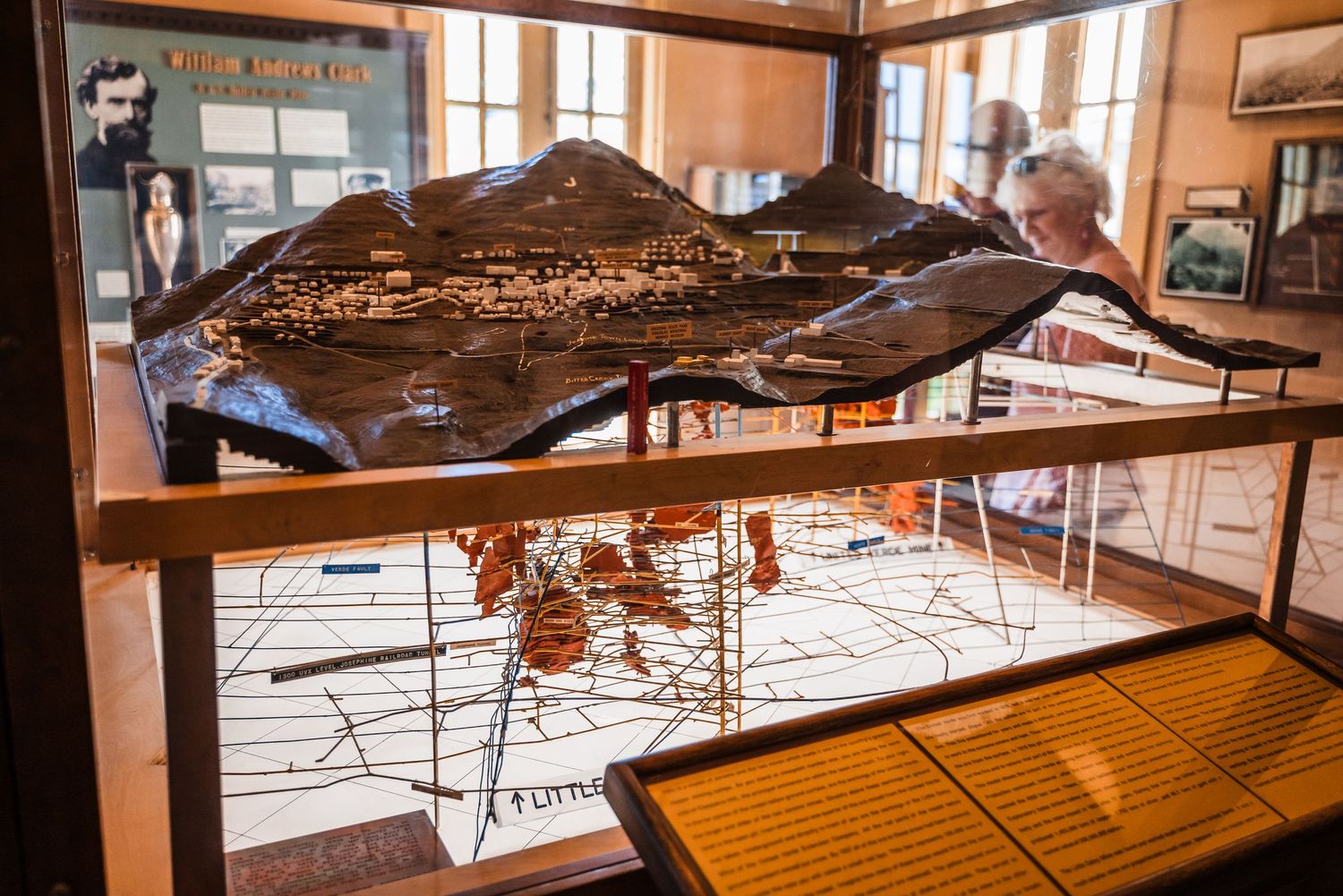 A topographical model display shows a mountainous landscape in a wood-framed museum case with maps underneath.