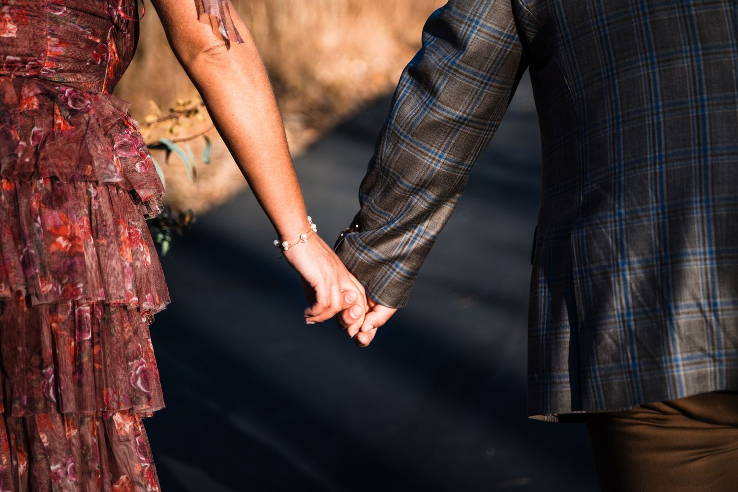 Close-up of couple holding hands showing burgundy dress and plaid jacket details.