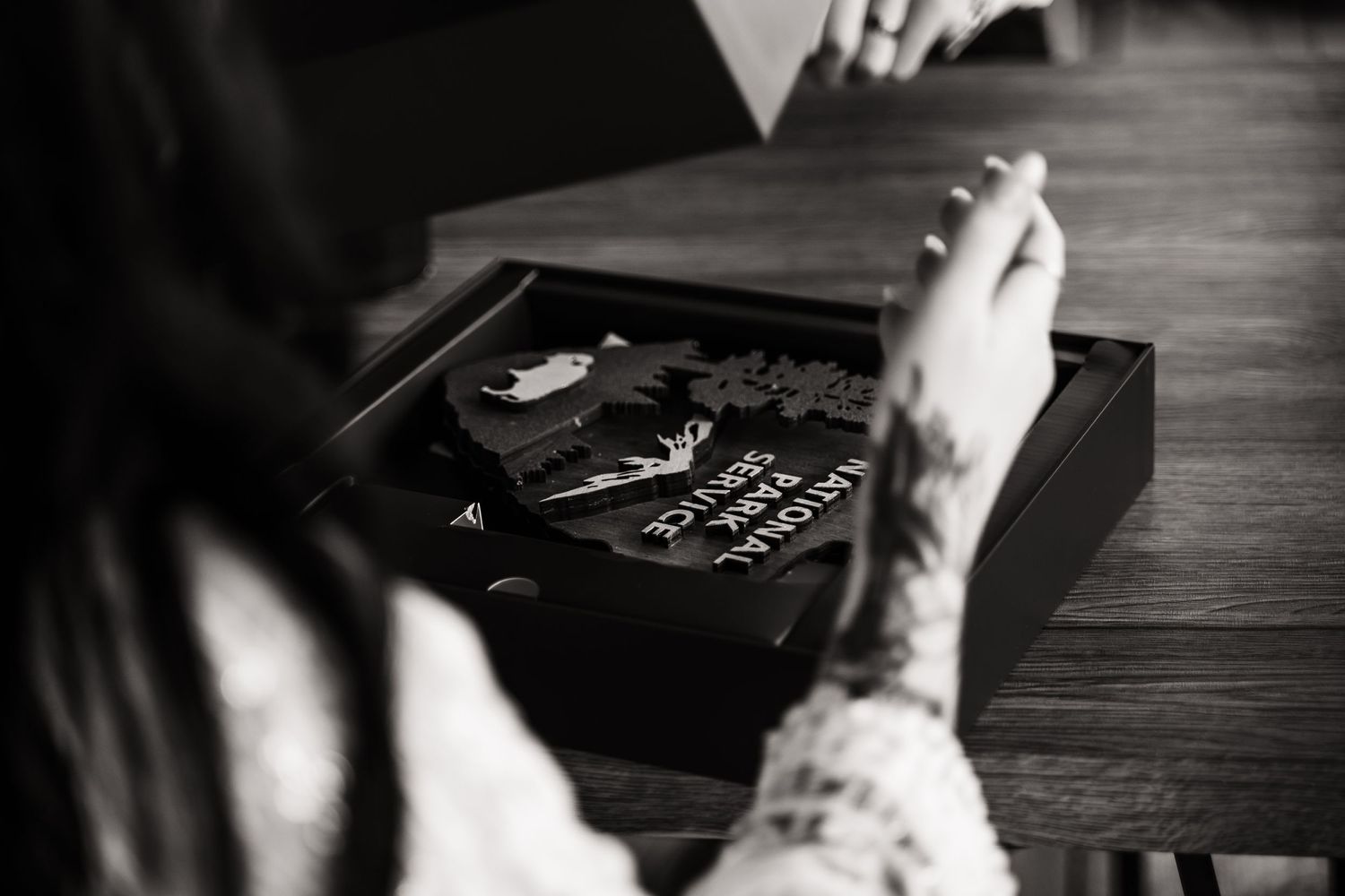 Black and white photo of hands opening a box or album on wooden surface.