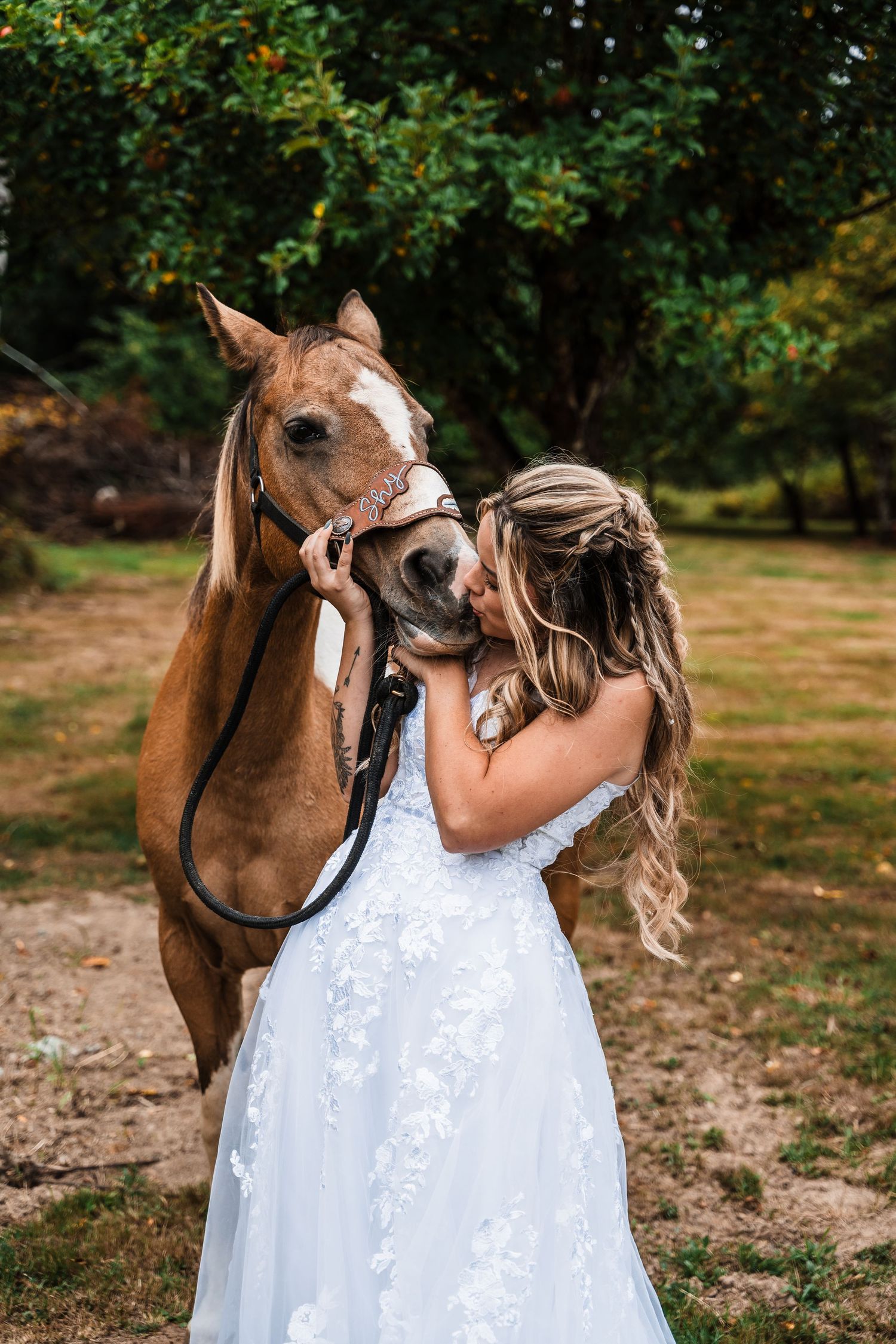 A white wedding dress contrasts against a brown horse's face in an intimate moment.