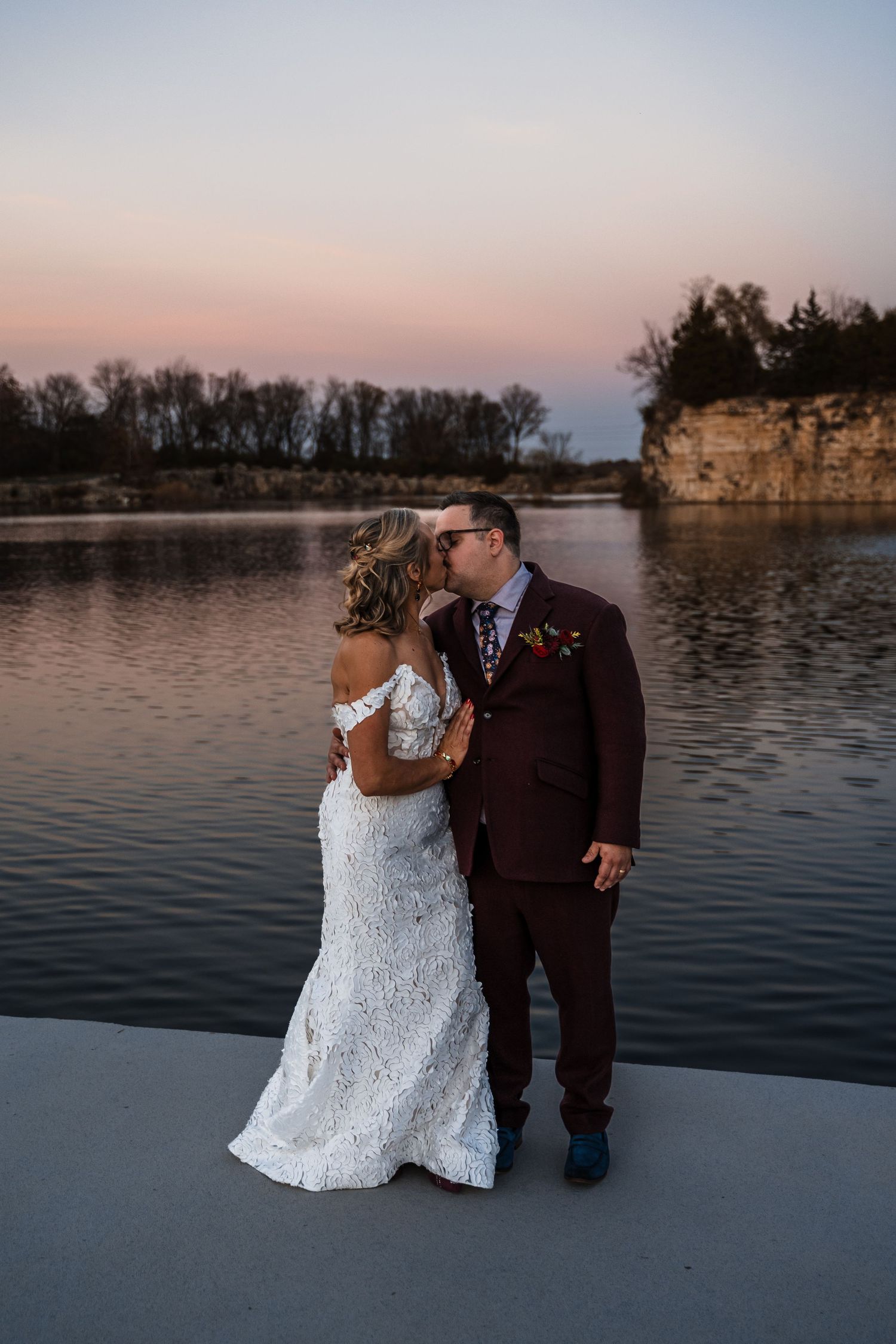 Newlyweds share intimate moment by quarry lake during sunset.