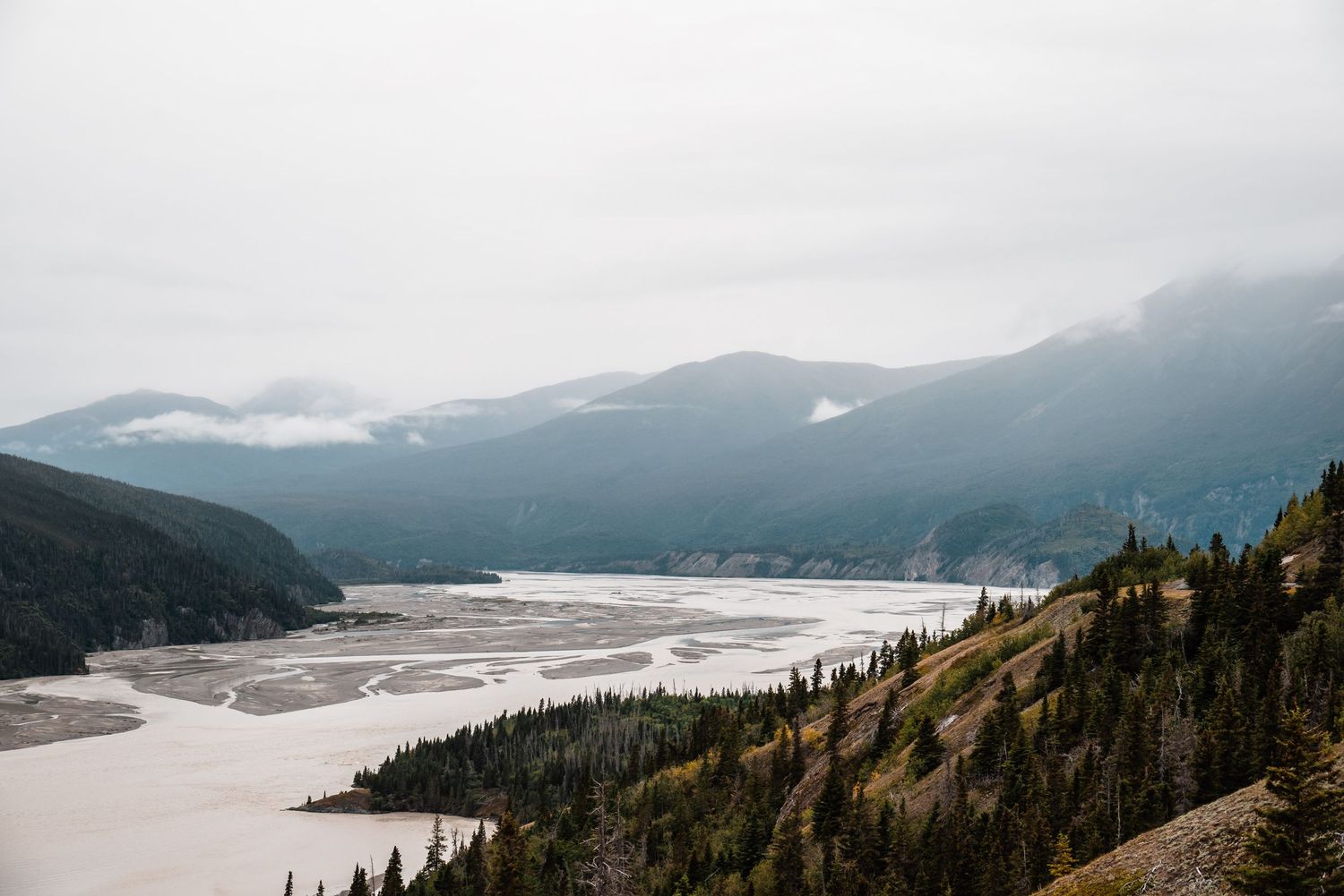 Misty mountain valley with a winding river below and evergreen forests covering the hillsides.