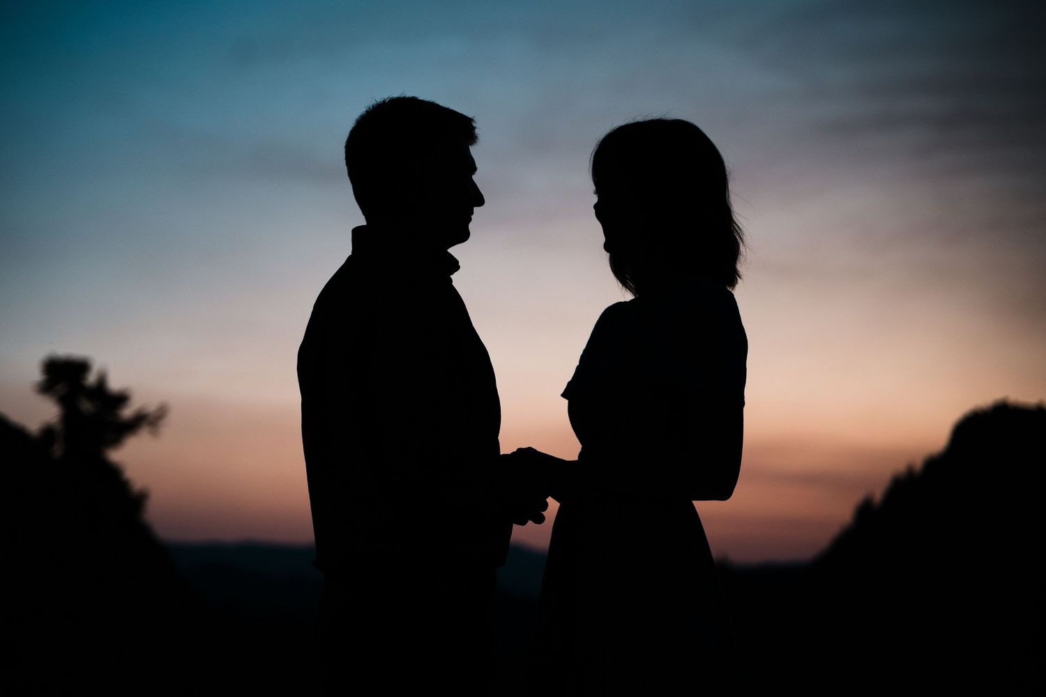 Silhouettes of a couple standing close together against a dramatic sunset sky.