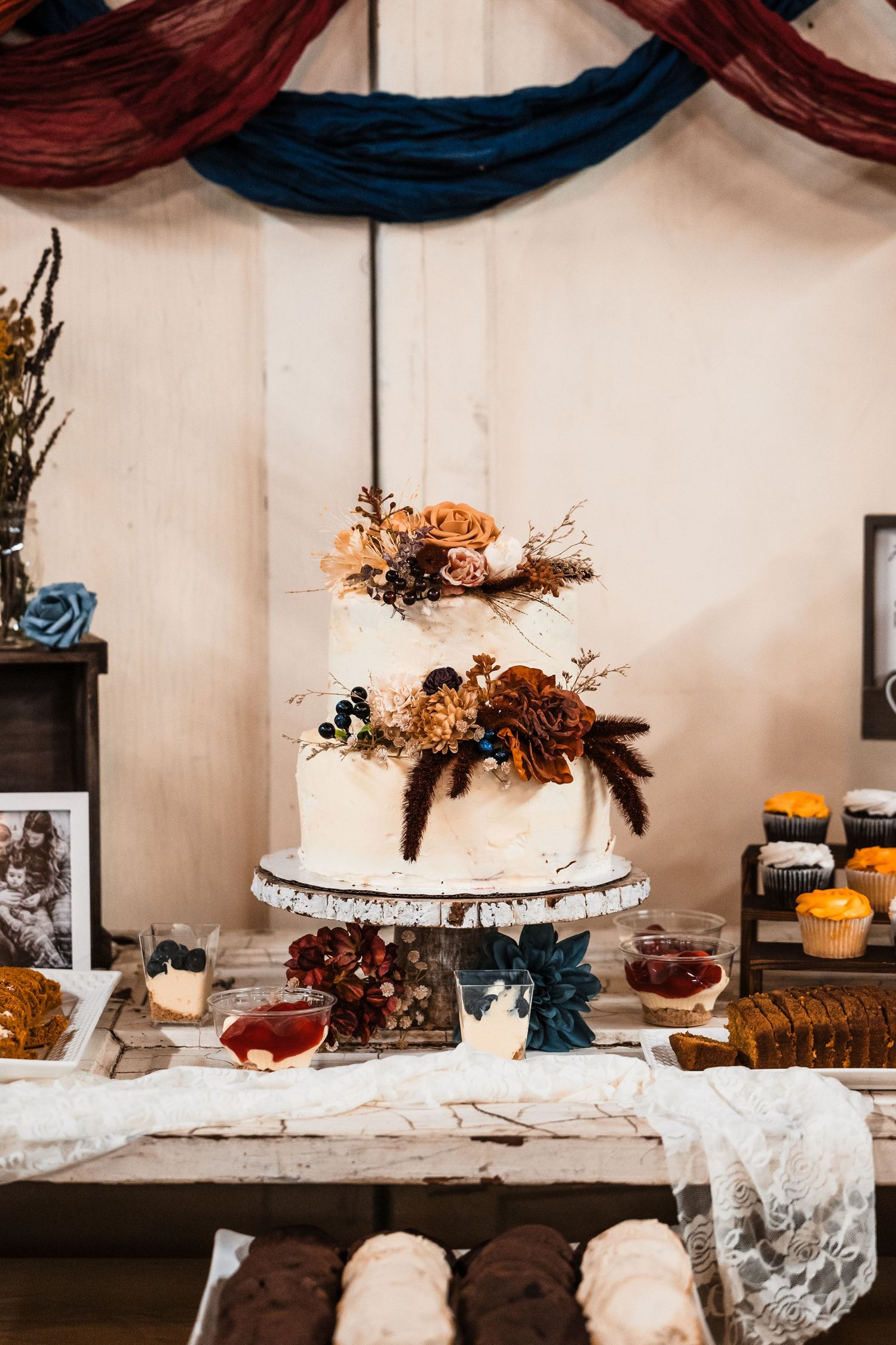 Elegant wedding dessert table with white cake and fall-themed decor against draped fabric backdrop.