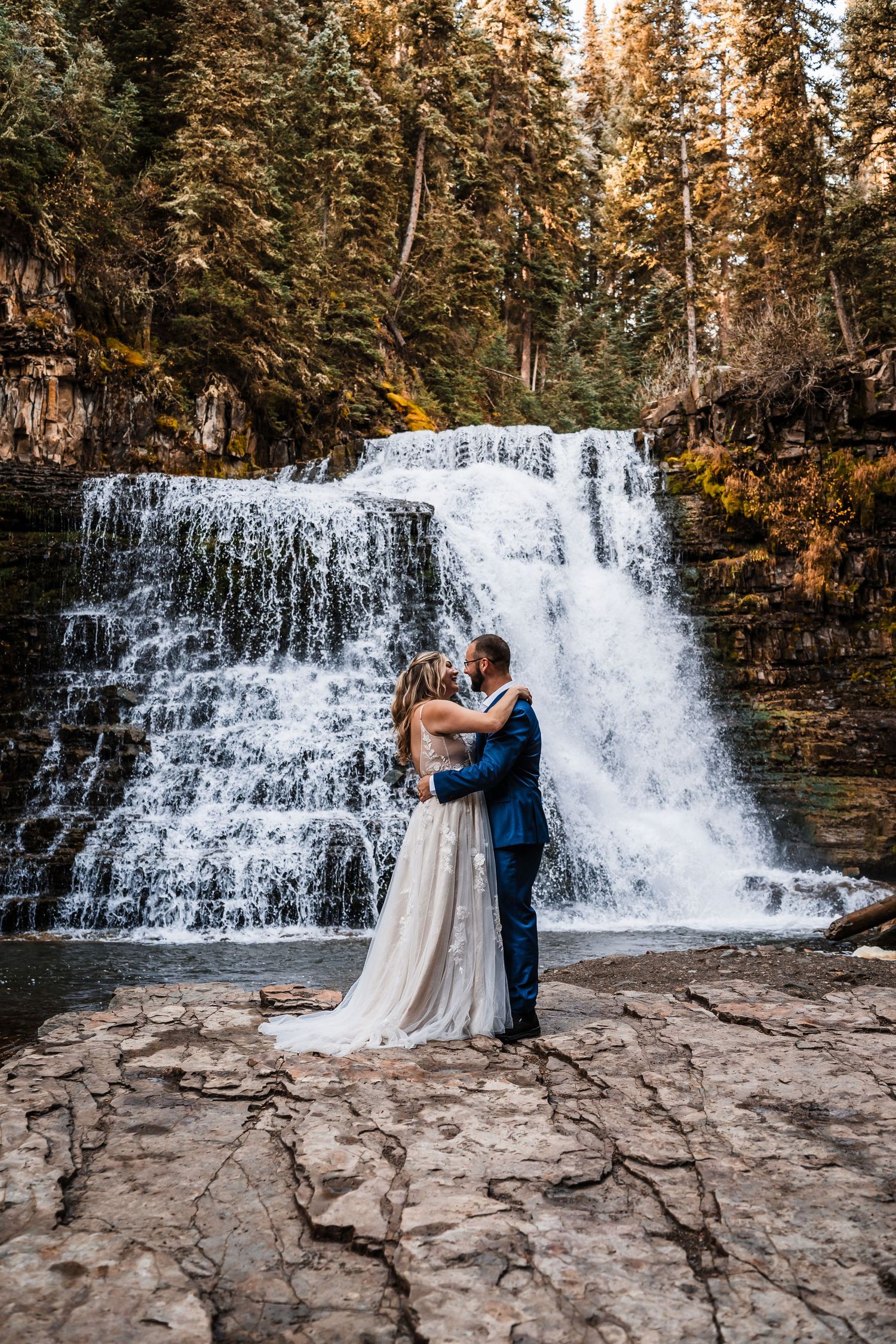 A romantic wedding photoshoot sequence in front of a cascading waterfall with rocky terrain.
