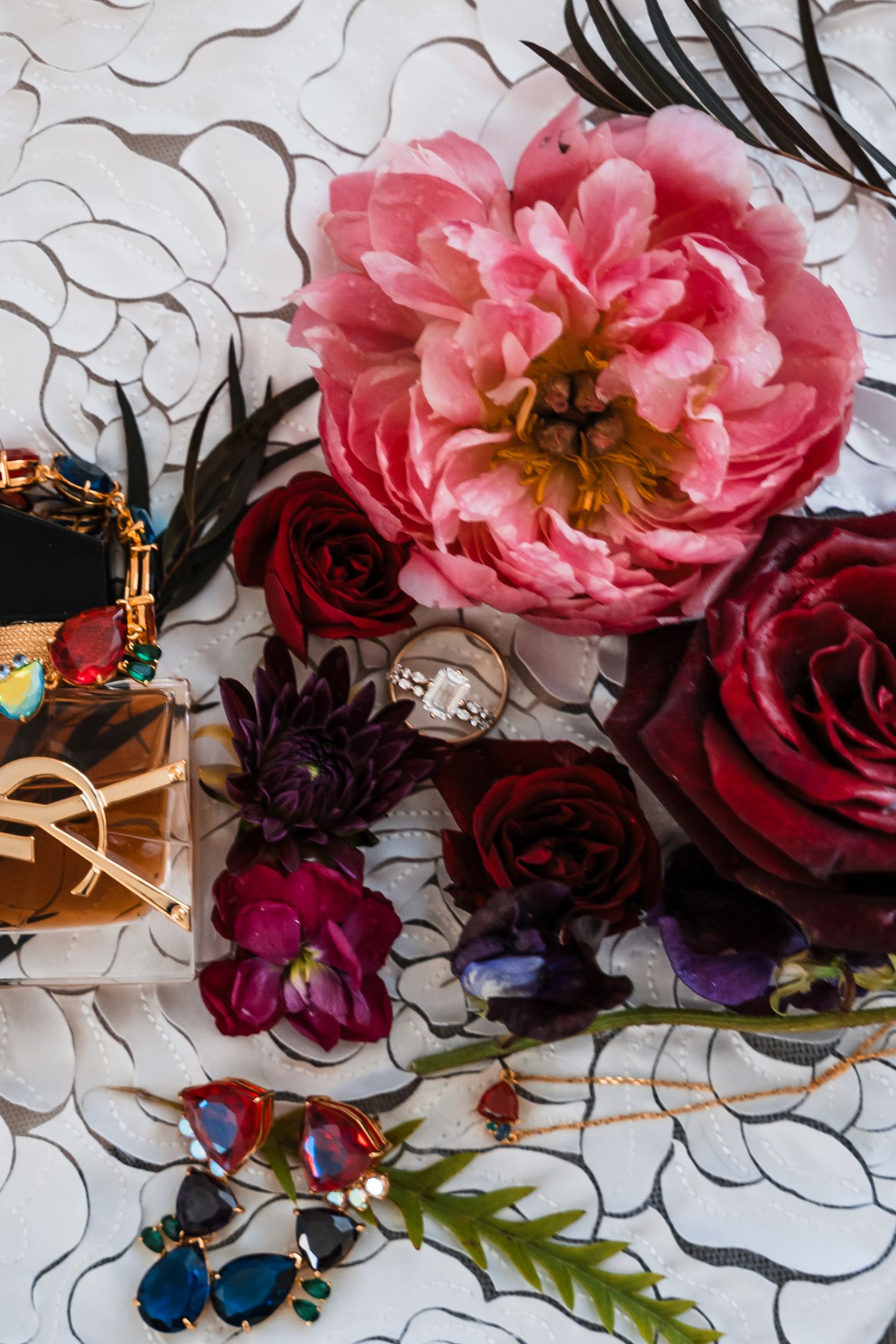 Wedding detail shot of pink and burgundy roses with decorative elements on a patterned background.