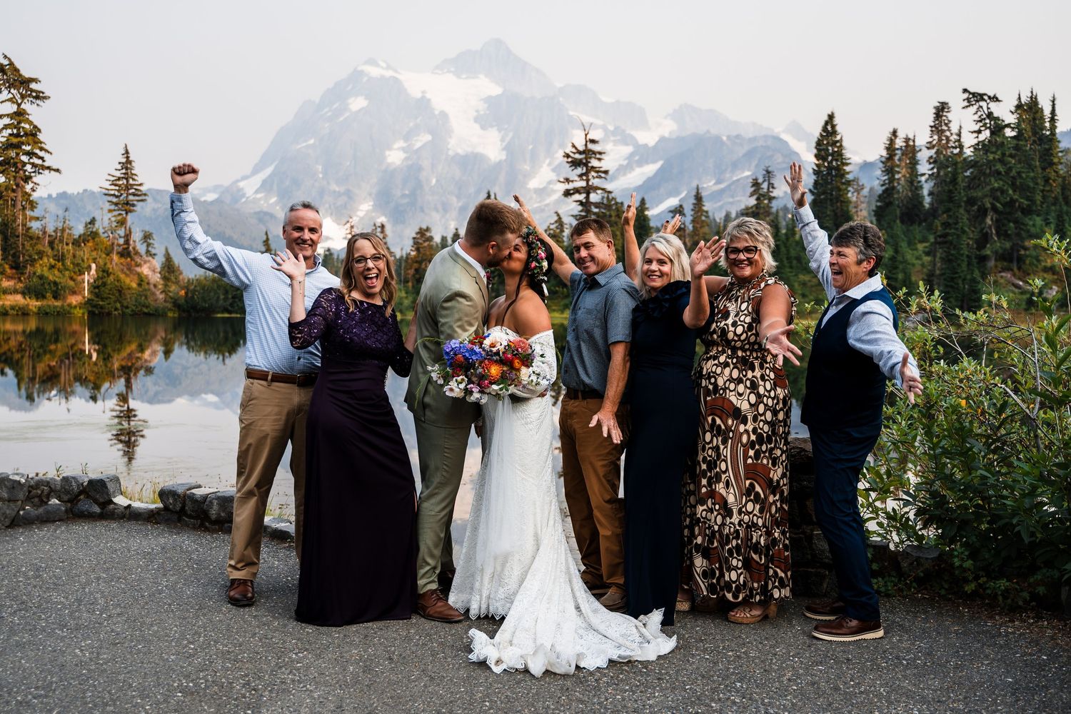 Wedding guests gather for group photos with majestic mountains and evergreen forest in the background.