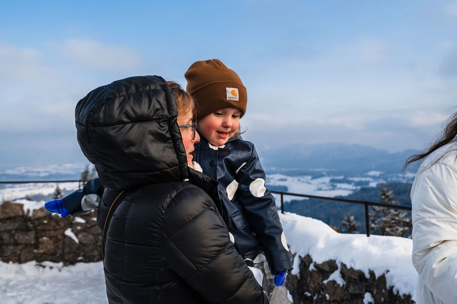 People explore a snow-covered mountain viewpoint overlooking a scenic winter landscape.