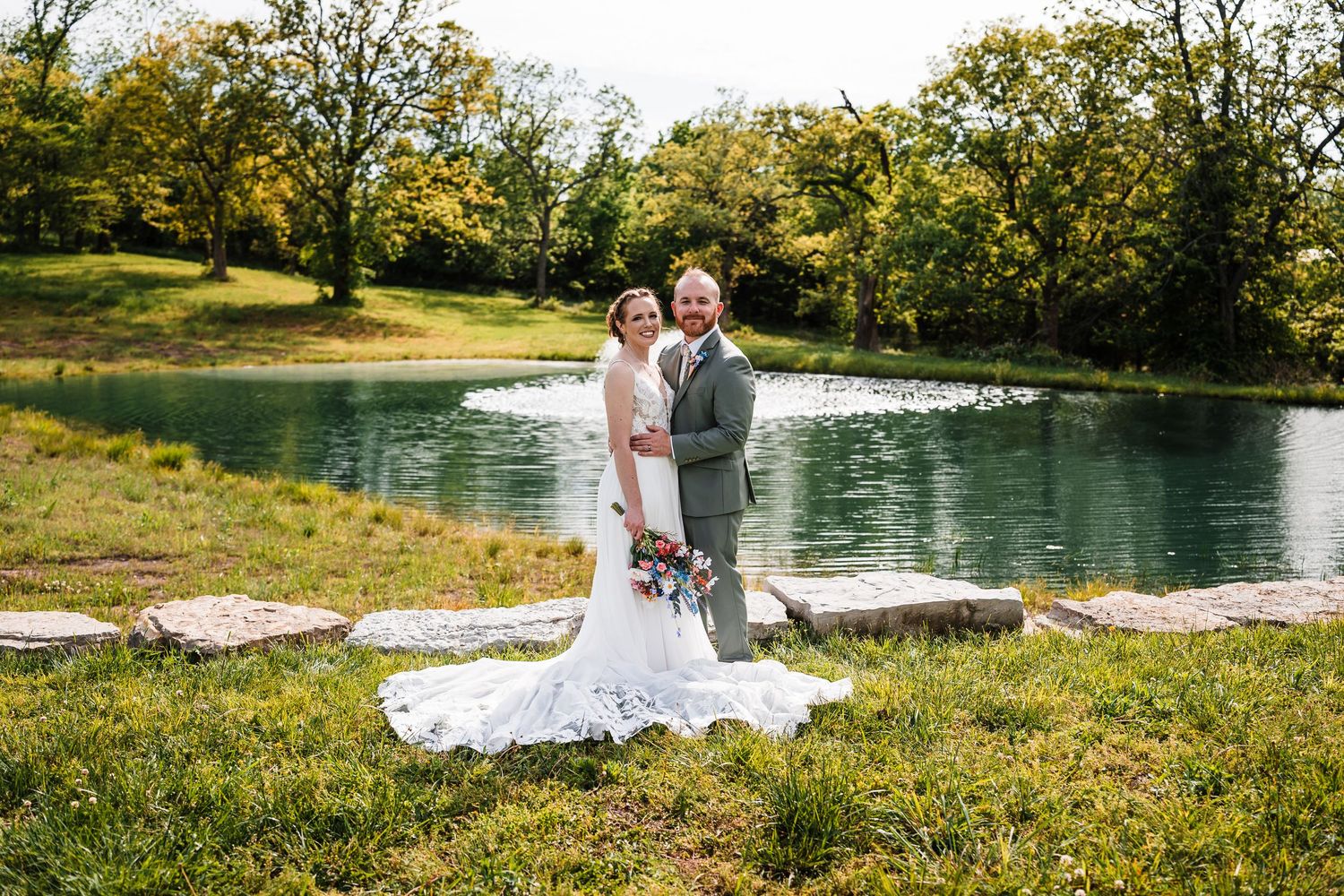 Bride and groom pose together in front of a tranquil pond on their wedding day.