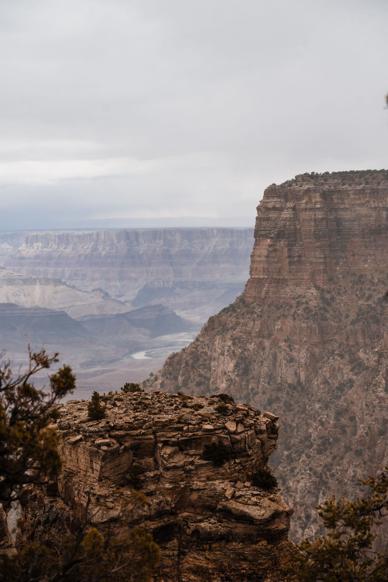 Dramatic view of the Grand Canyon's layered rock formations and cliffs under an overcast sky.