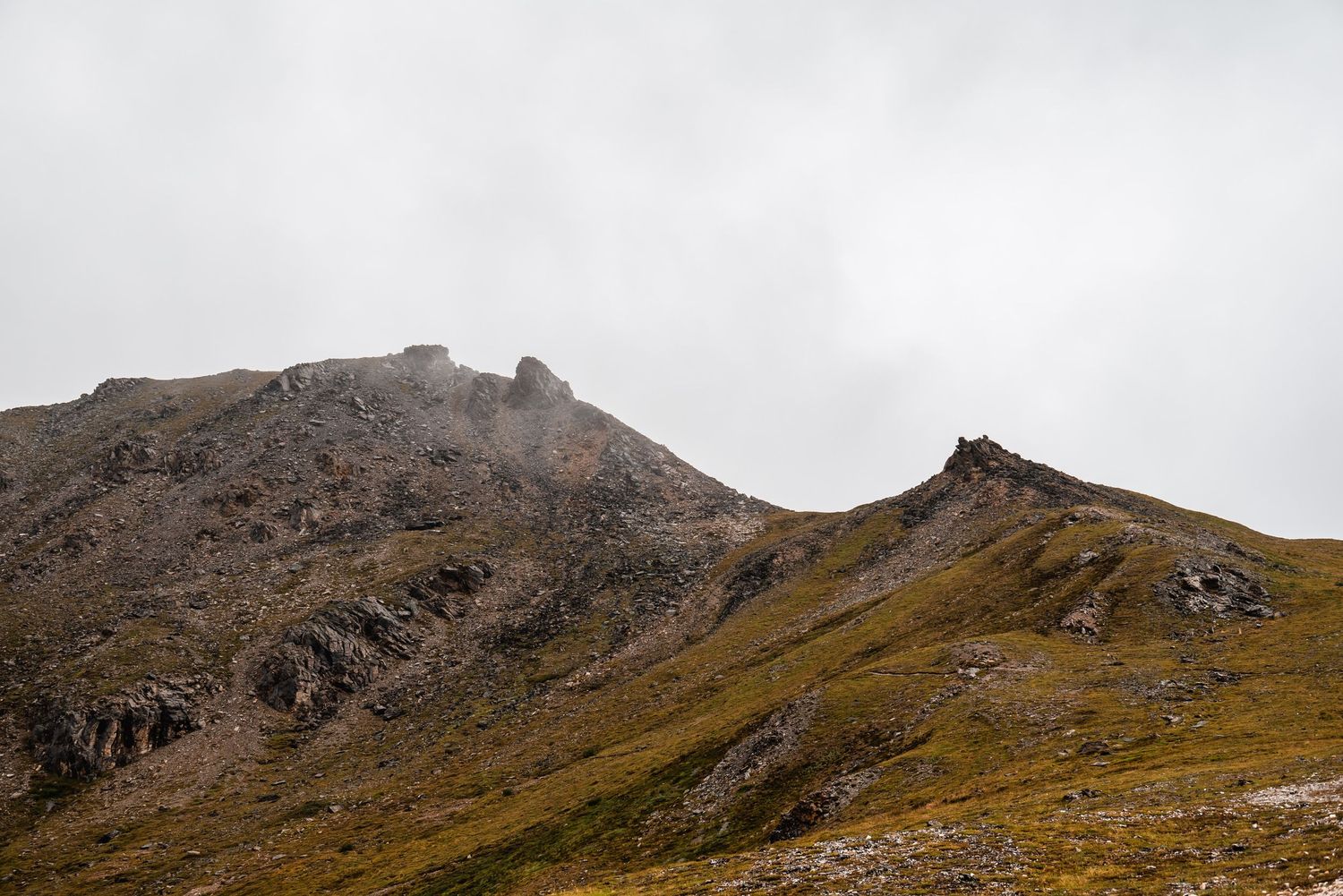 Rugged mountain landscape with rocky peaks and golden slopes under an overcast sky.