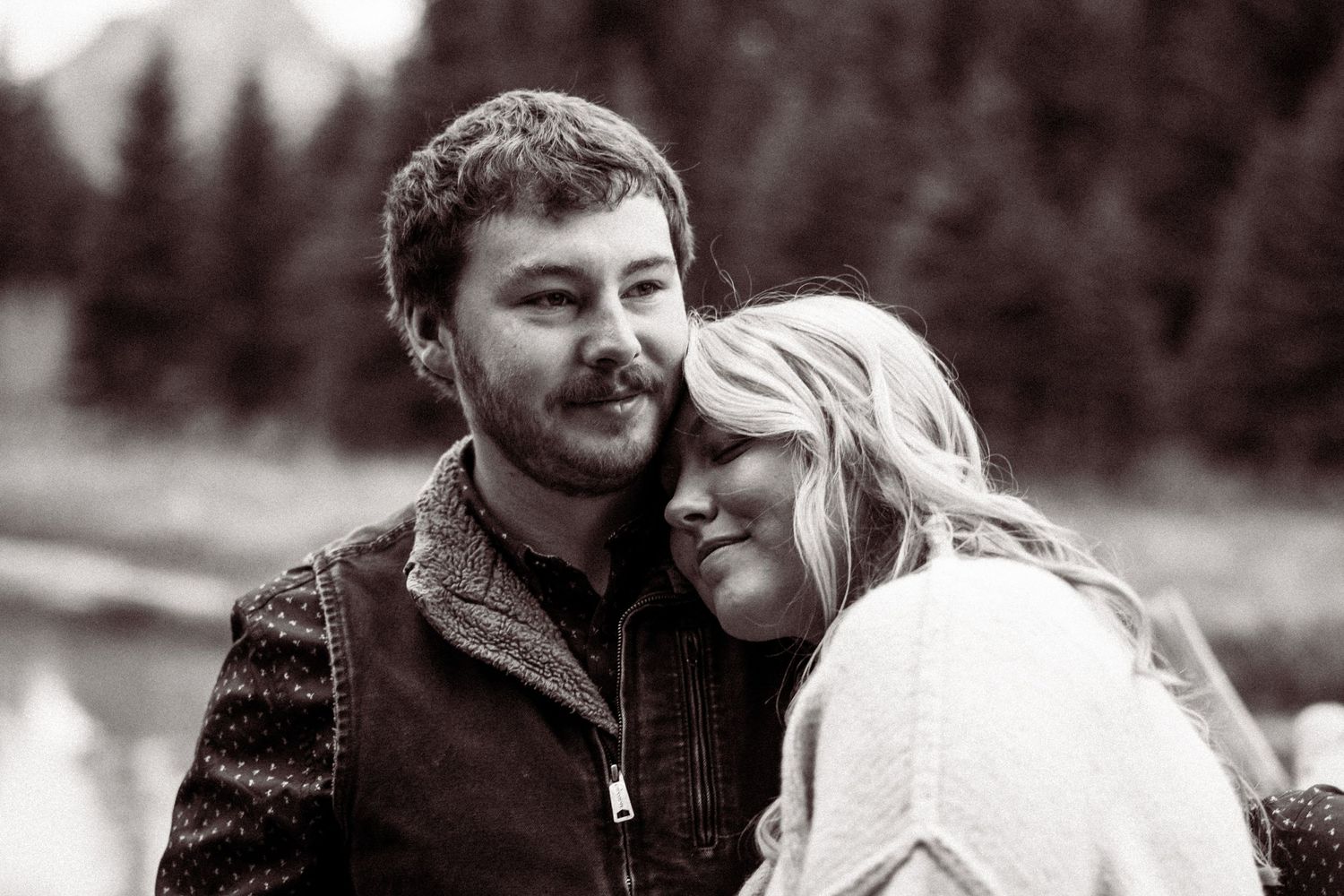 A series of black and white romantic photos showing a couple embracing outdoors in a natural setting.
