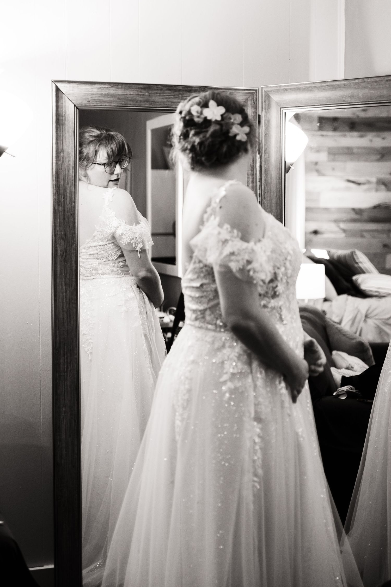Black and white photo of a bride looking in a mirror showing the delicate lace details of her wedding gown.