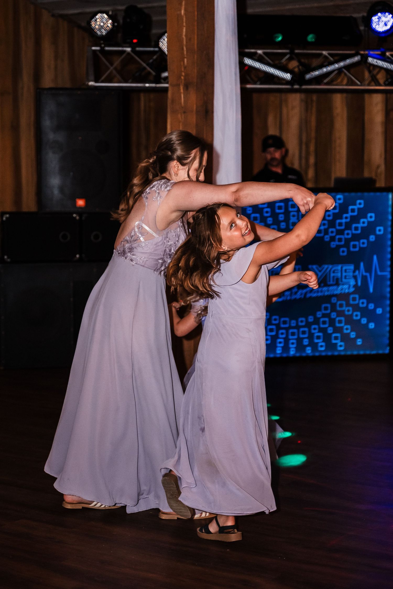 Two dancers in matching lavender dresses twirl together on a dimly lit dance floor.
