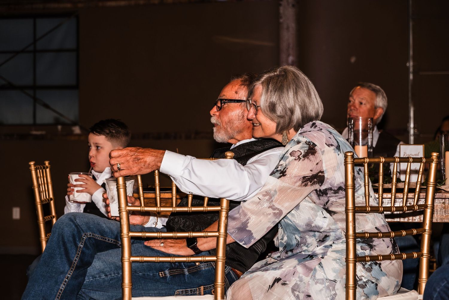 Guests enjoying a celebration at tables with gold chiavari chairs in a dimly lit venue.