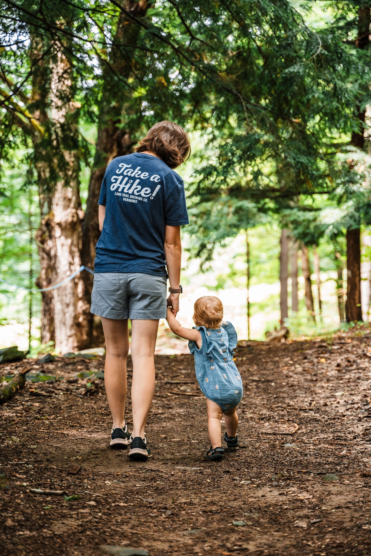 Adult and child walking hand in hand along a wooded hiking trail.