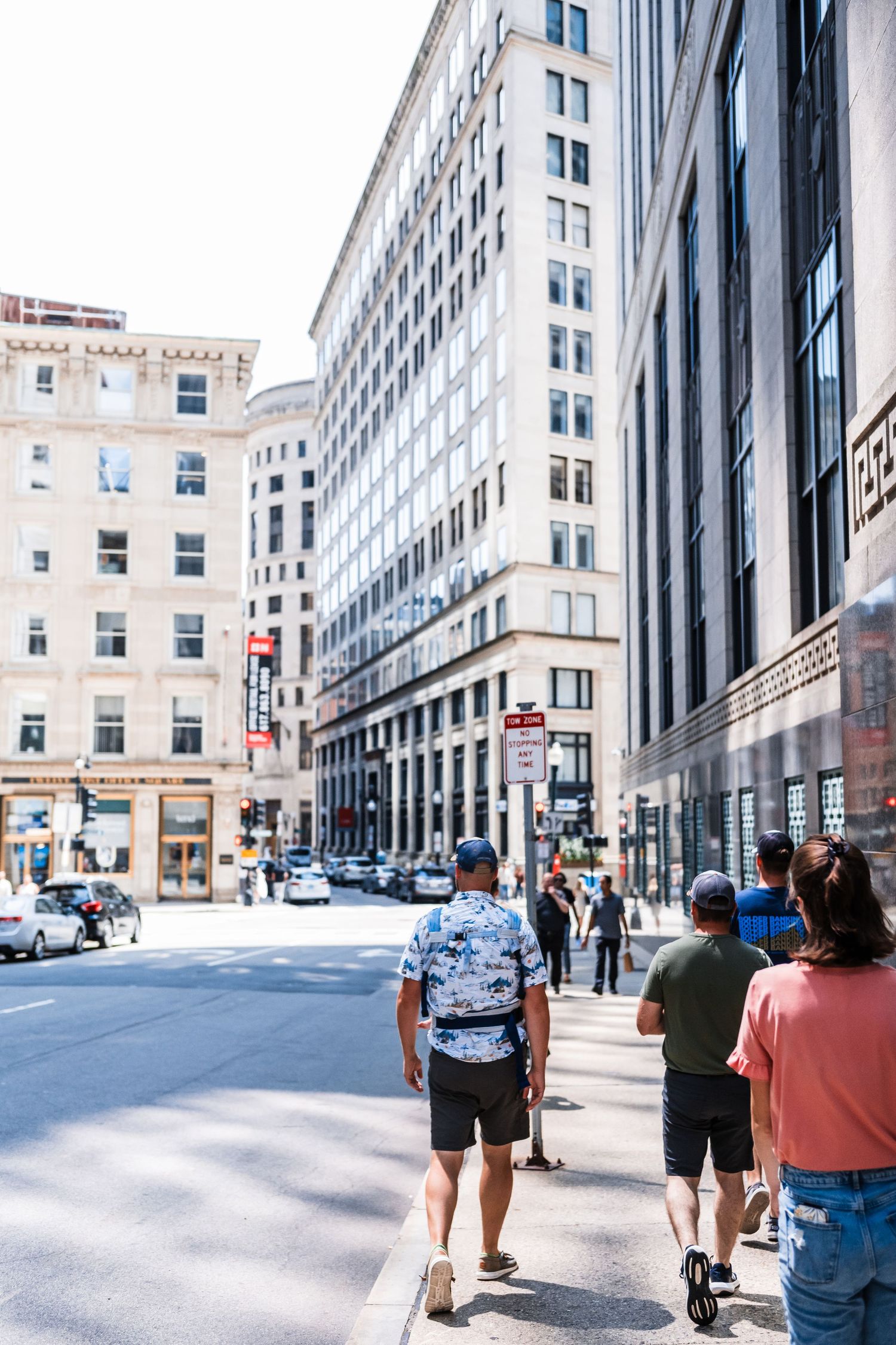 People walking on a busy downtown sidewalk with tall commercial buildings and storefronts in Boston.