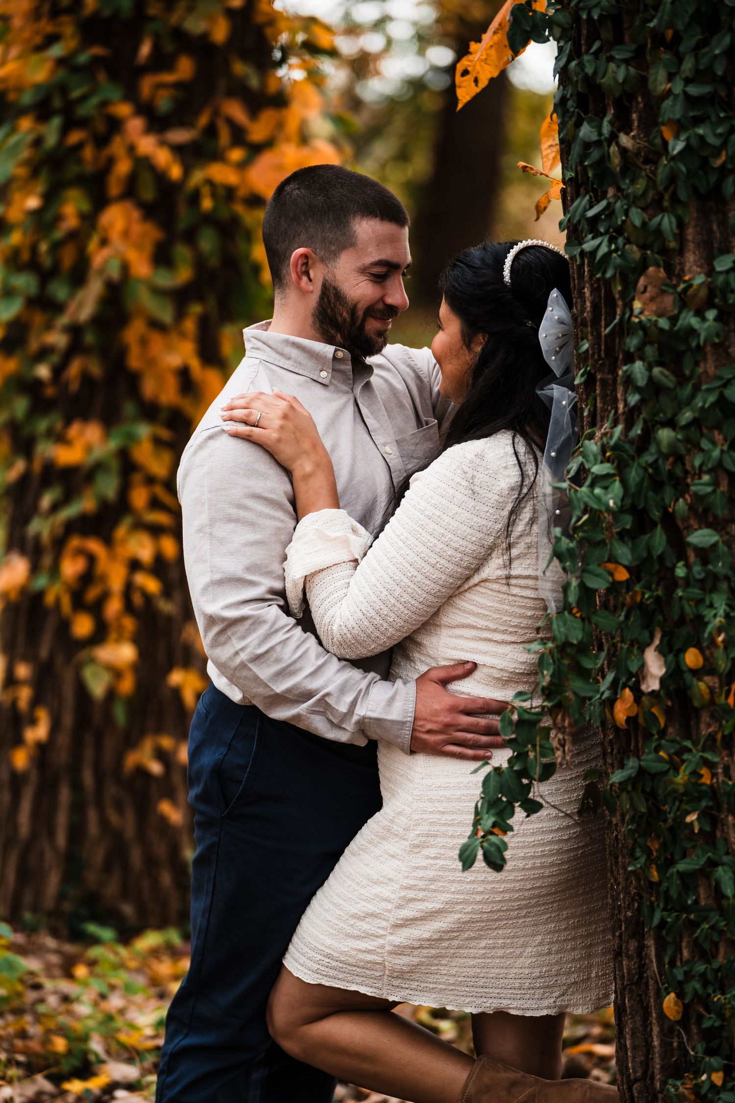 Couple embracing against tree with autumn colors in background.