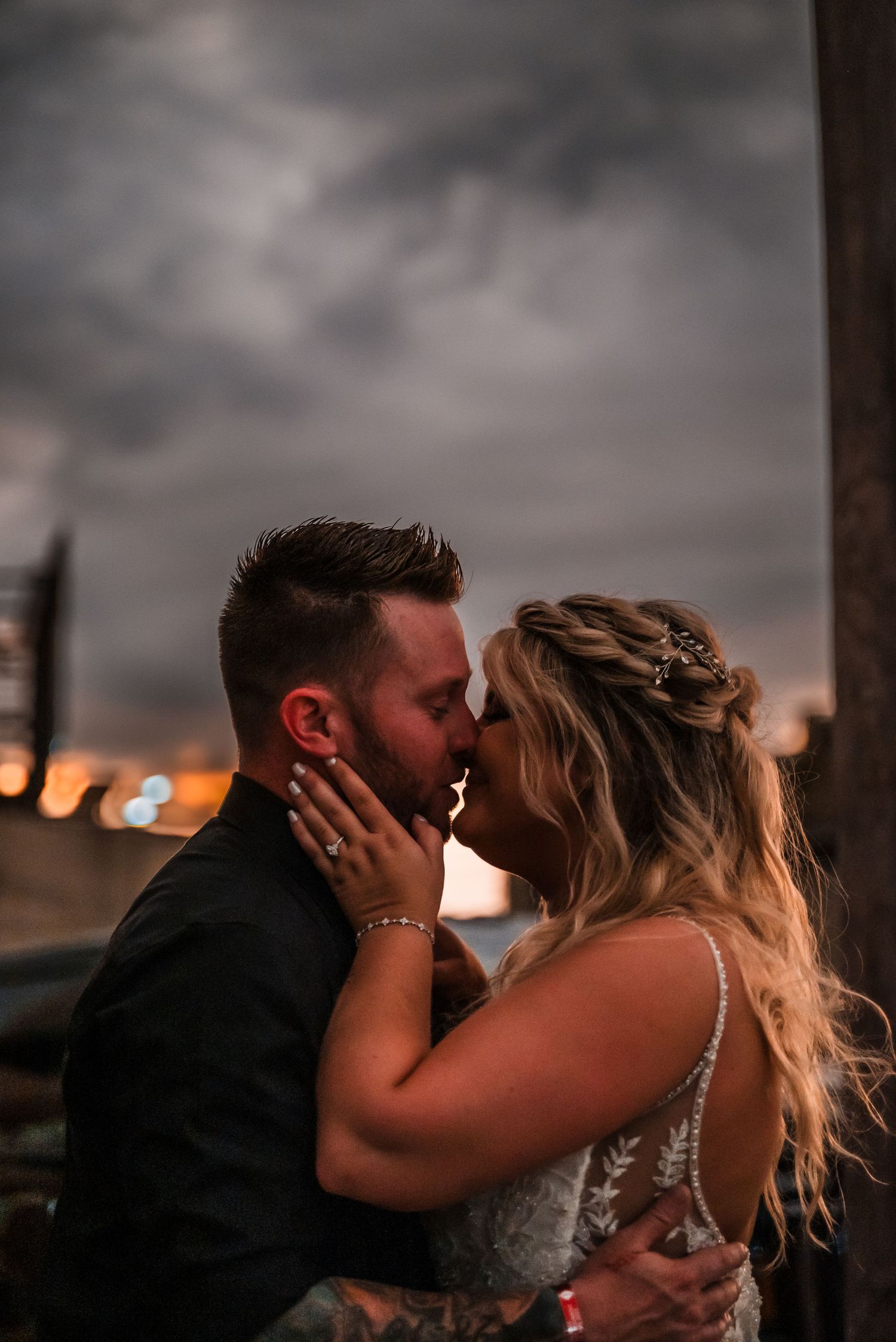 Romantic couple sharing an intimate kiss at sunset with dramatic cloudy sky in the background.