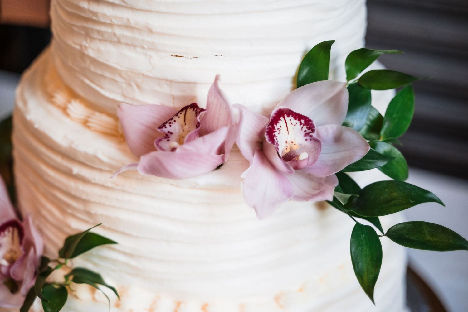 Close-up of a white tiered wedding cake decorated with delicate pink orchids and green foliage.