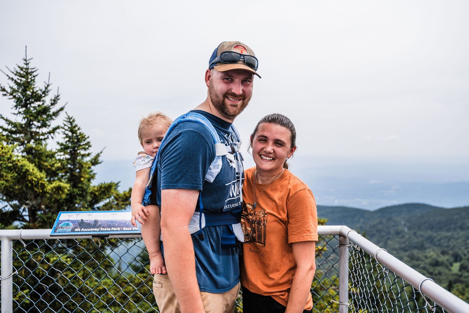 Happy group posing on an observation deck overlooking mountain scenery on a cloudy day.