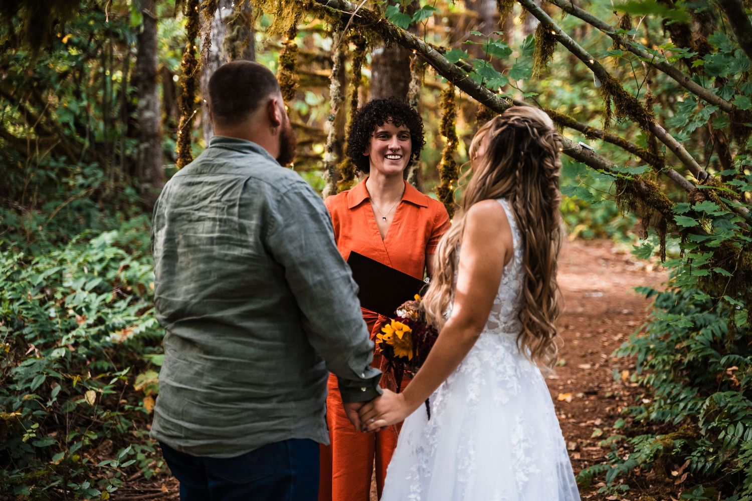 Wedding ceremony taking place on a wooded trail with officiant in bright orange attire.