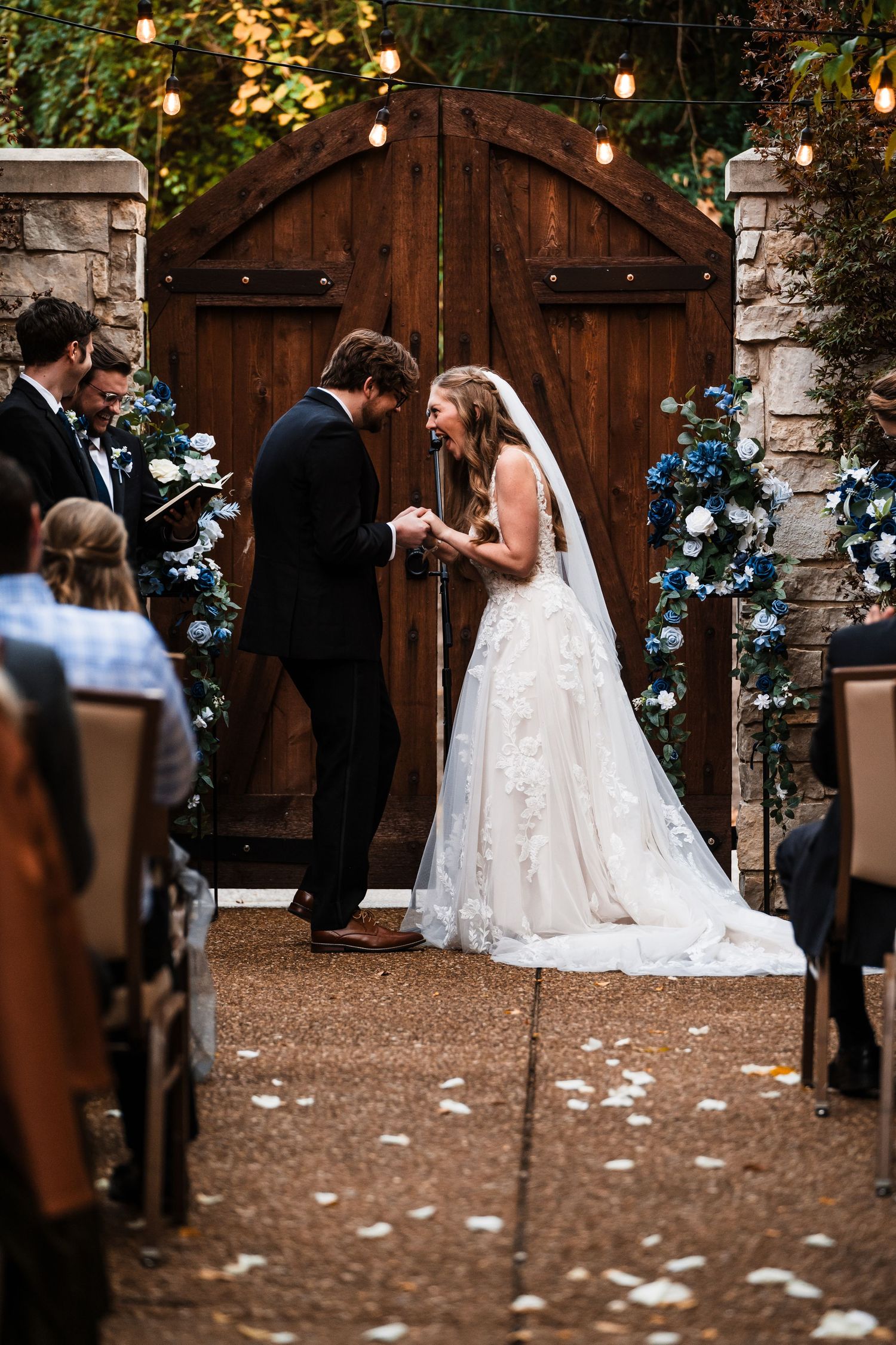 Intimate wedding ceremony moment in front of rustic wooden doors with floral decorations.