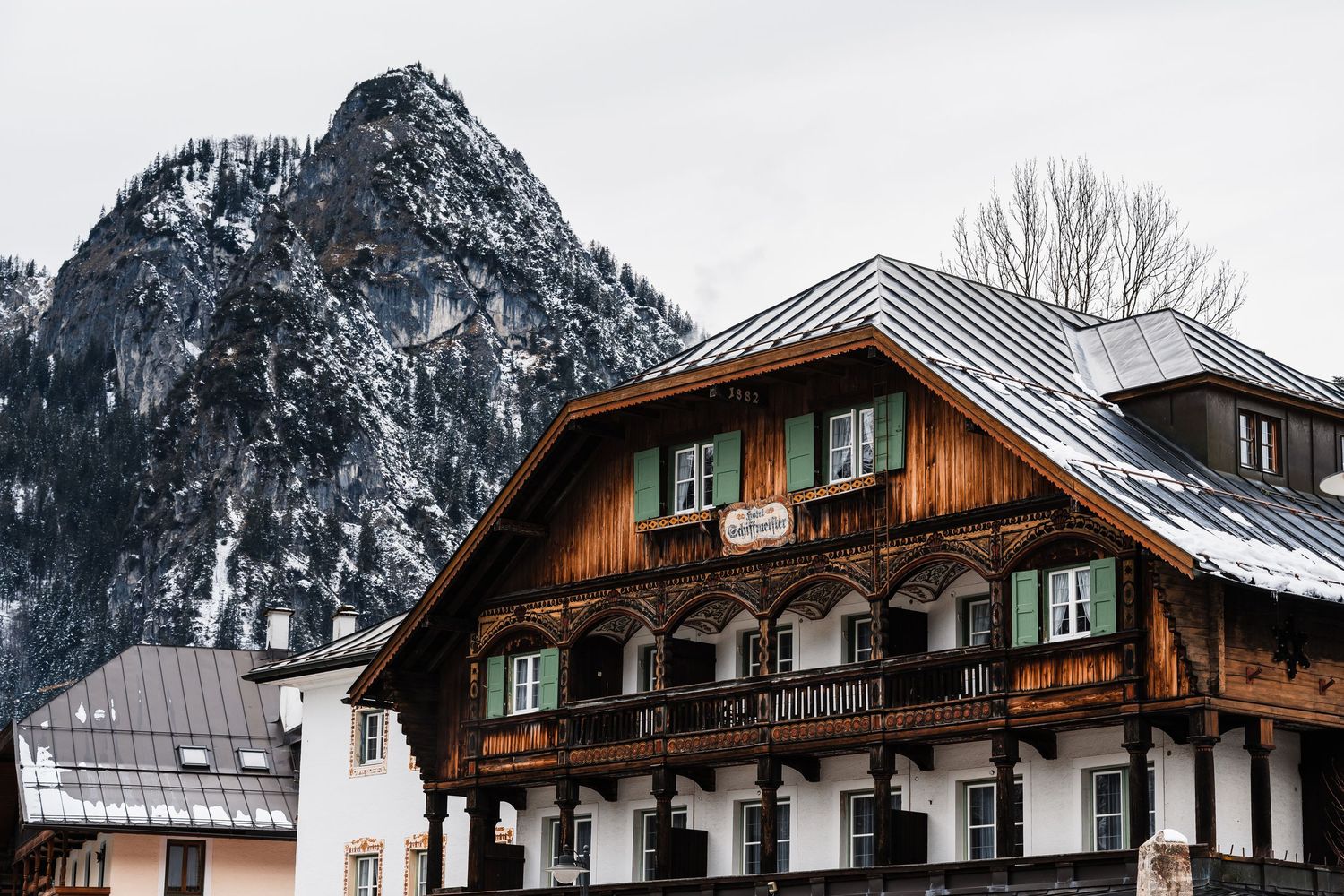 Snow-covered traditional Alpine chalet with green shutters nestled against dramatic mountain peaks in winter landscape.