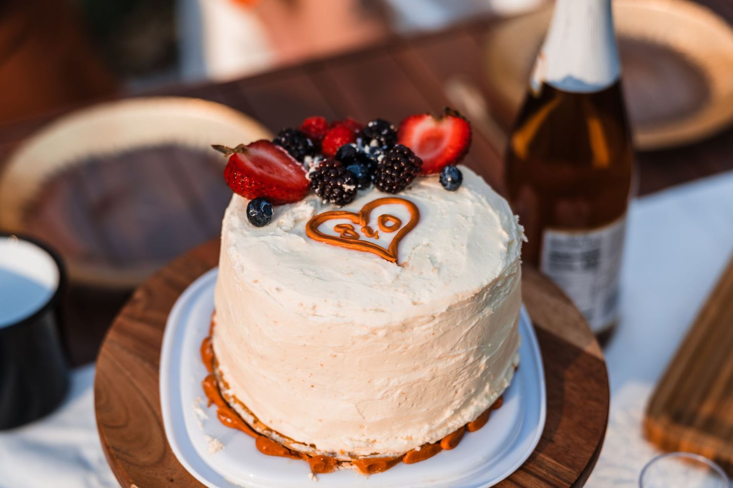 Elegant single-tier white frosted wedding cake topped with fresh strawberries, blackberries, and blueberries on wooden stand.