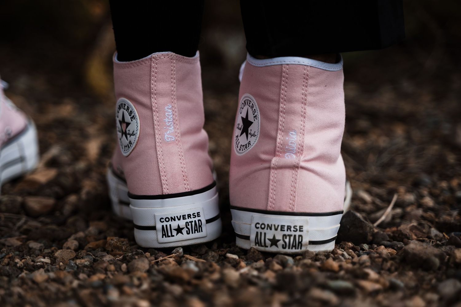 Close-up of pink Converse high-top sneakers on dirt ground.
